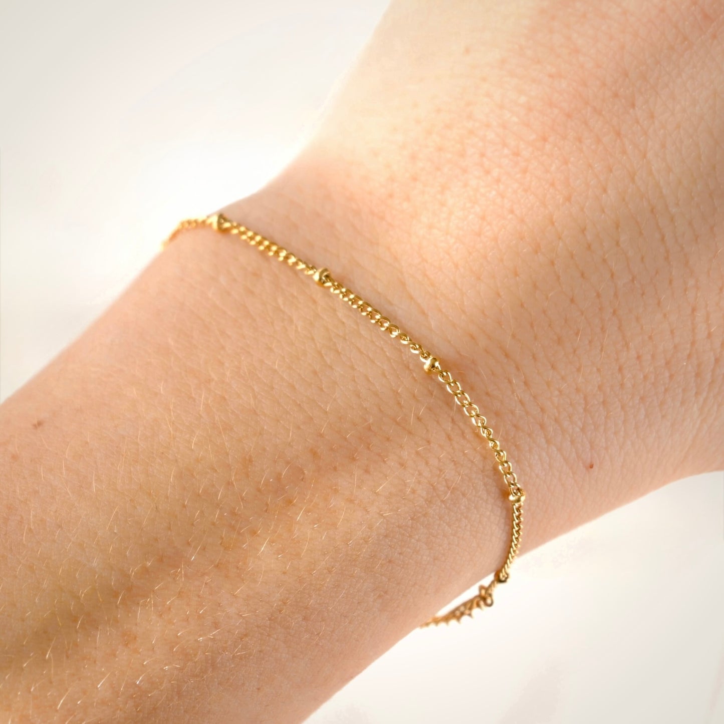 Gold  beaded chain bracelet on a wrist against a white background