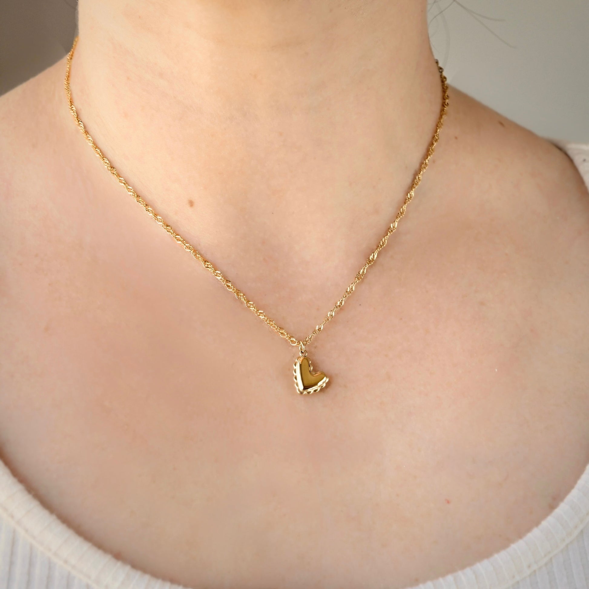 Gold necklace with a heart pendant on a person wearing a white sweater.