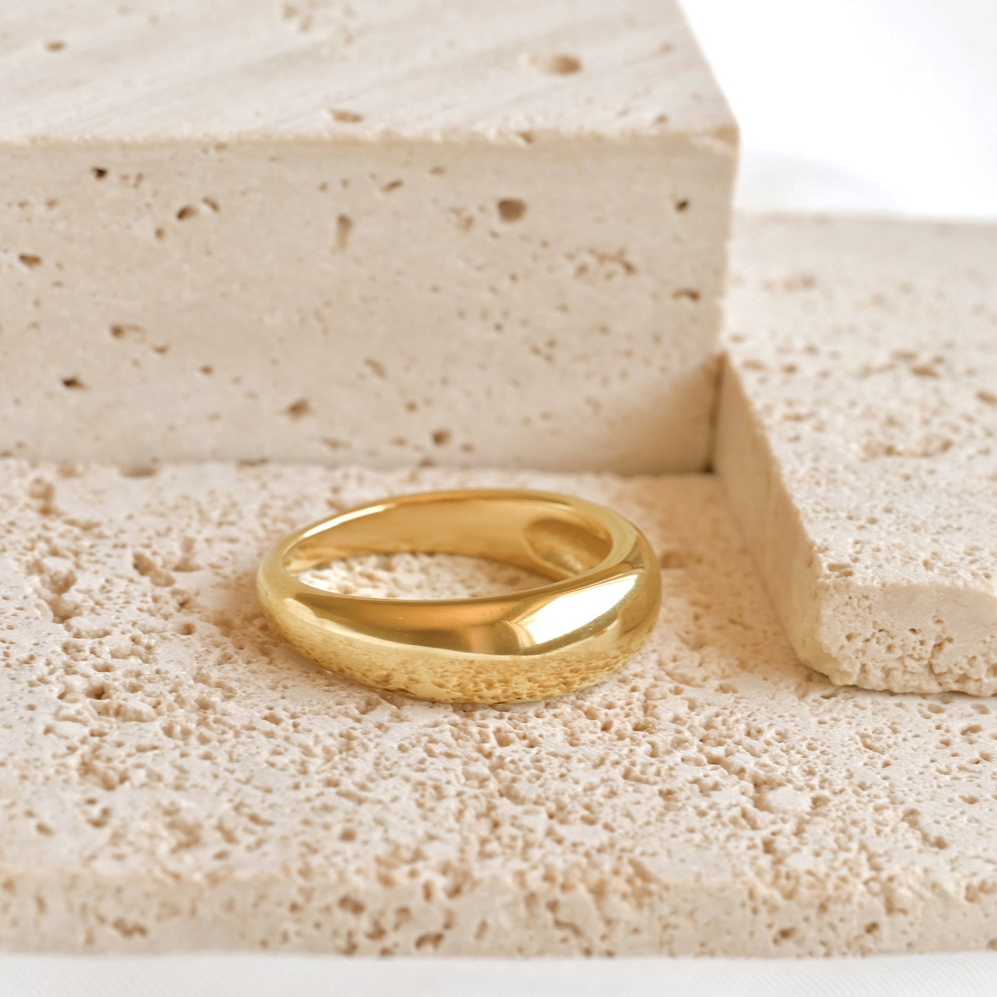 Gold plain dome ring on a textured beige surface