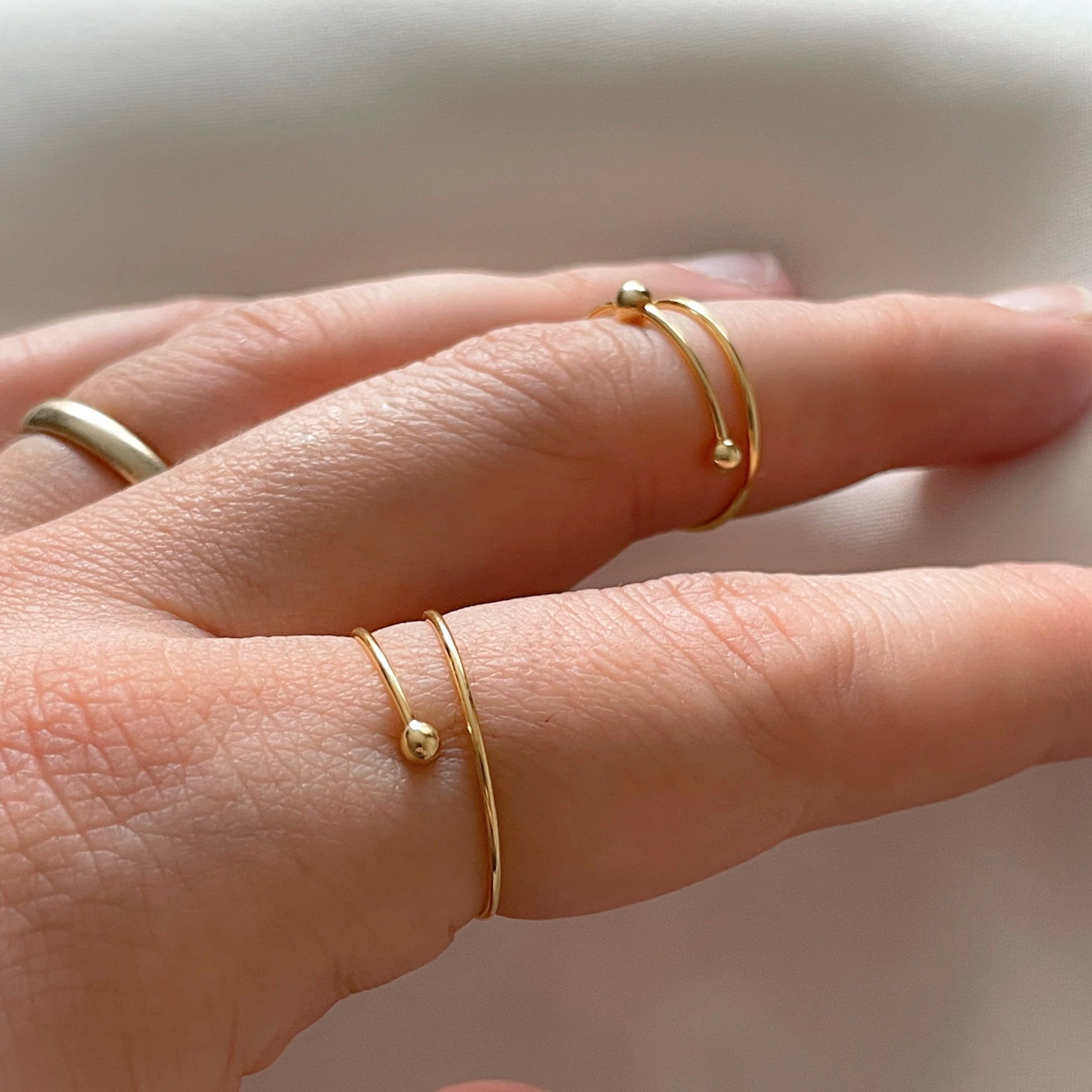 Two beaded gold wrap rings on a person's fingers against a neutral background
