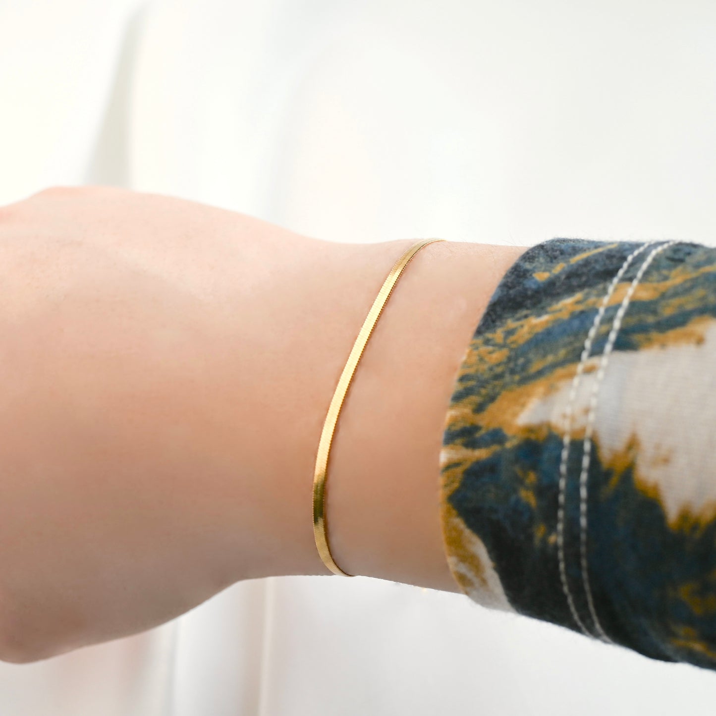 Gold  herringbone chain bracelet  reflecting light on a wrist with a blurred background