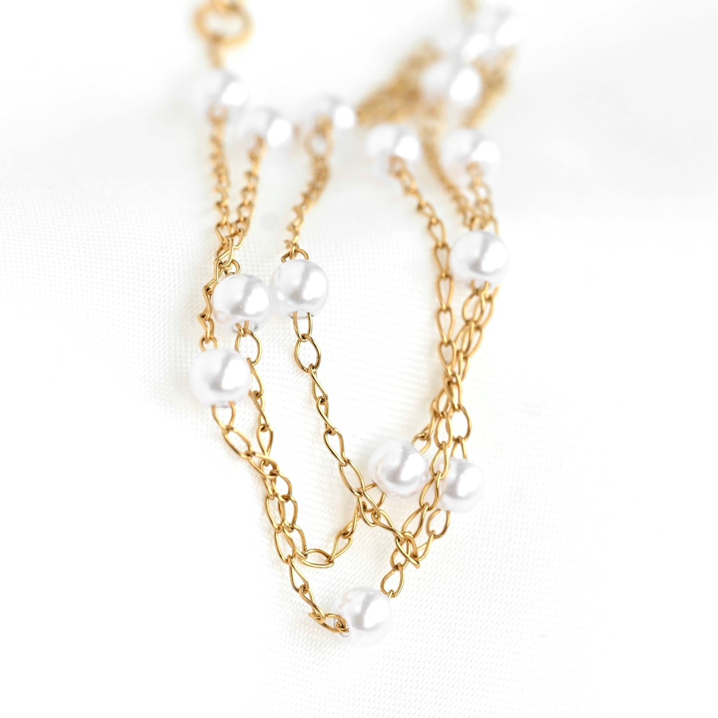 Gold chain necklace with white pearl beads on a light background