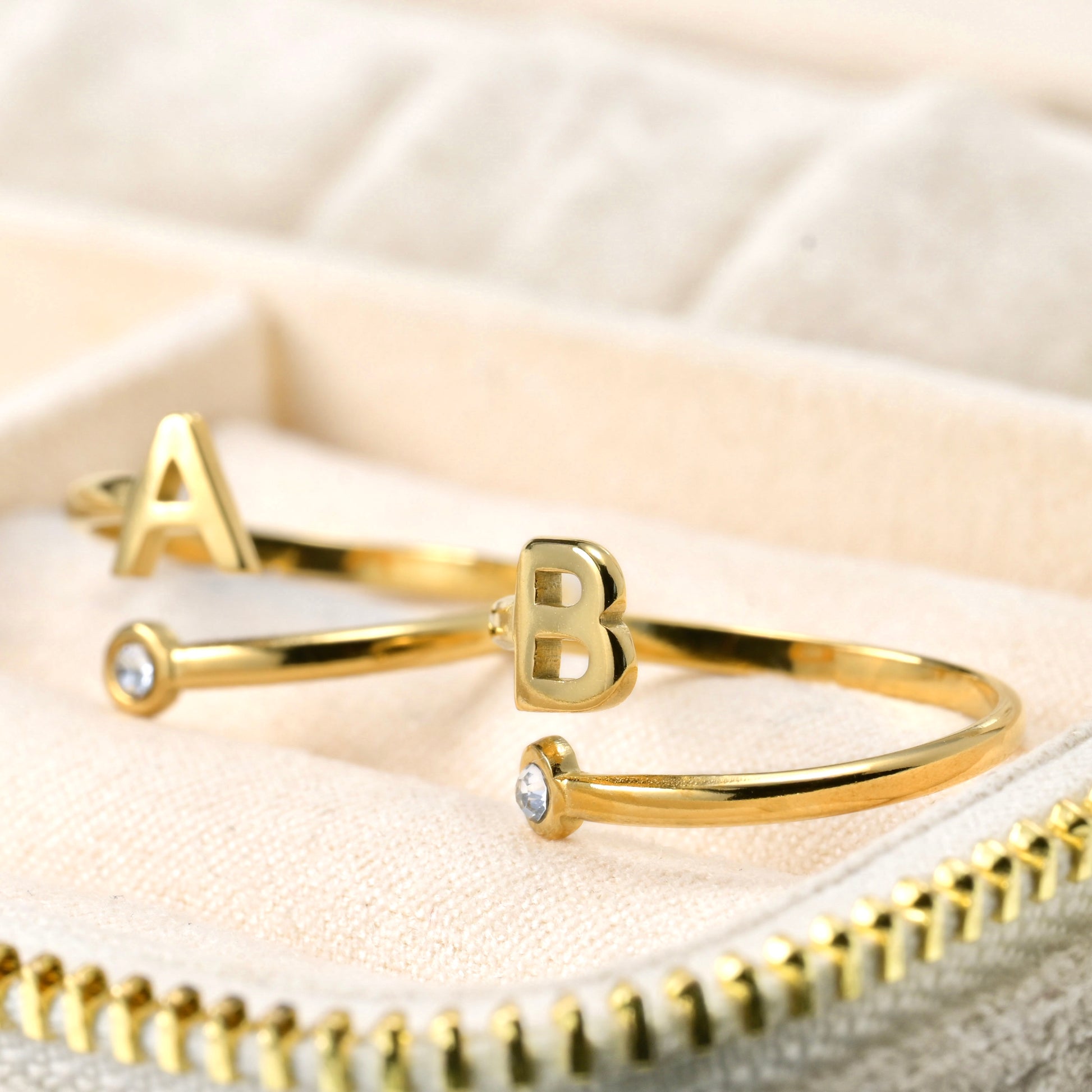 Thin Gold Wrap Rigns with letter 'A' and 'B' on a beige fabric background