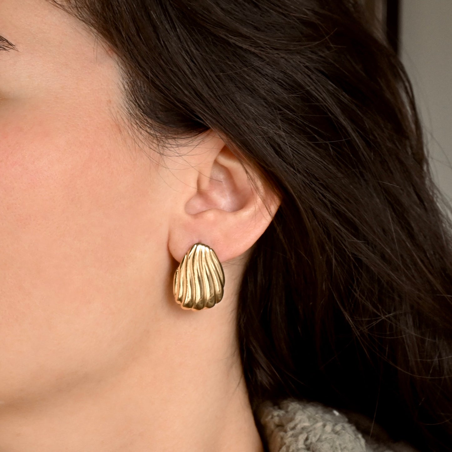 Close-up of a person wearing a gold seashell earrings with dark hair.