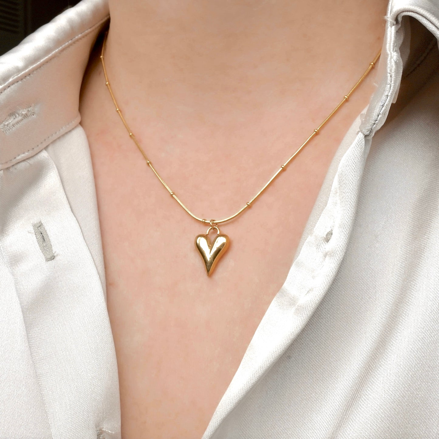 Angled view of gold puffy heart necklace worn by a person in a white shirt