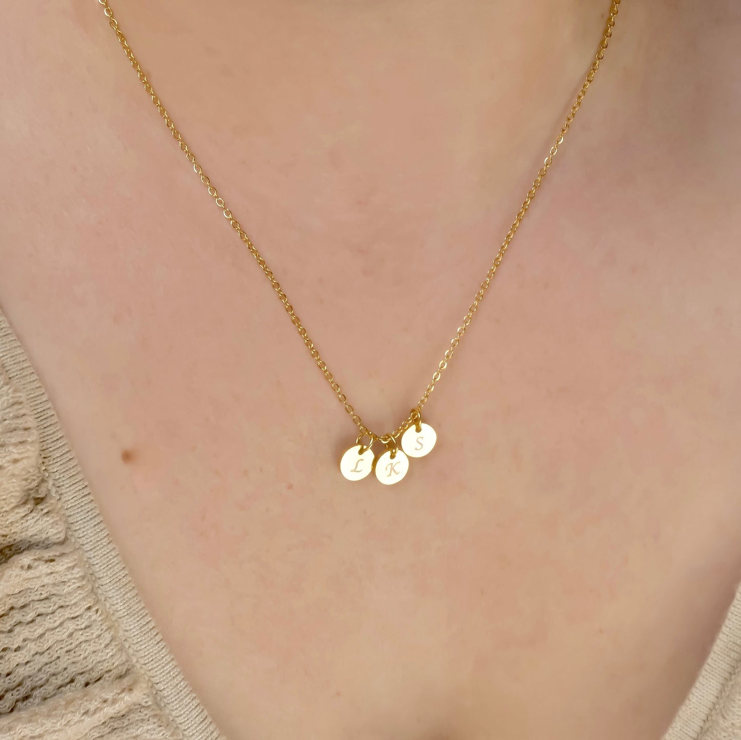 Gold necklace with three disc pendants reflecting light on a person wearing a beige top.