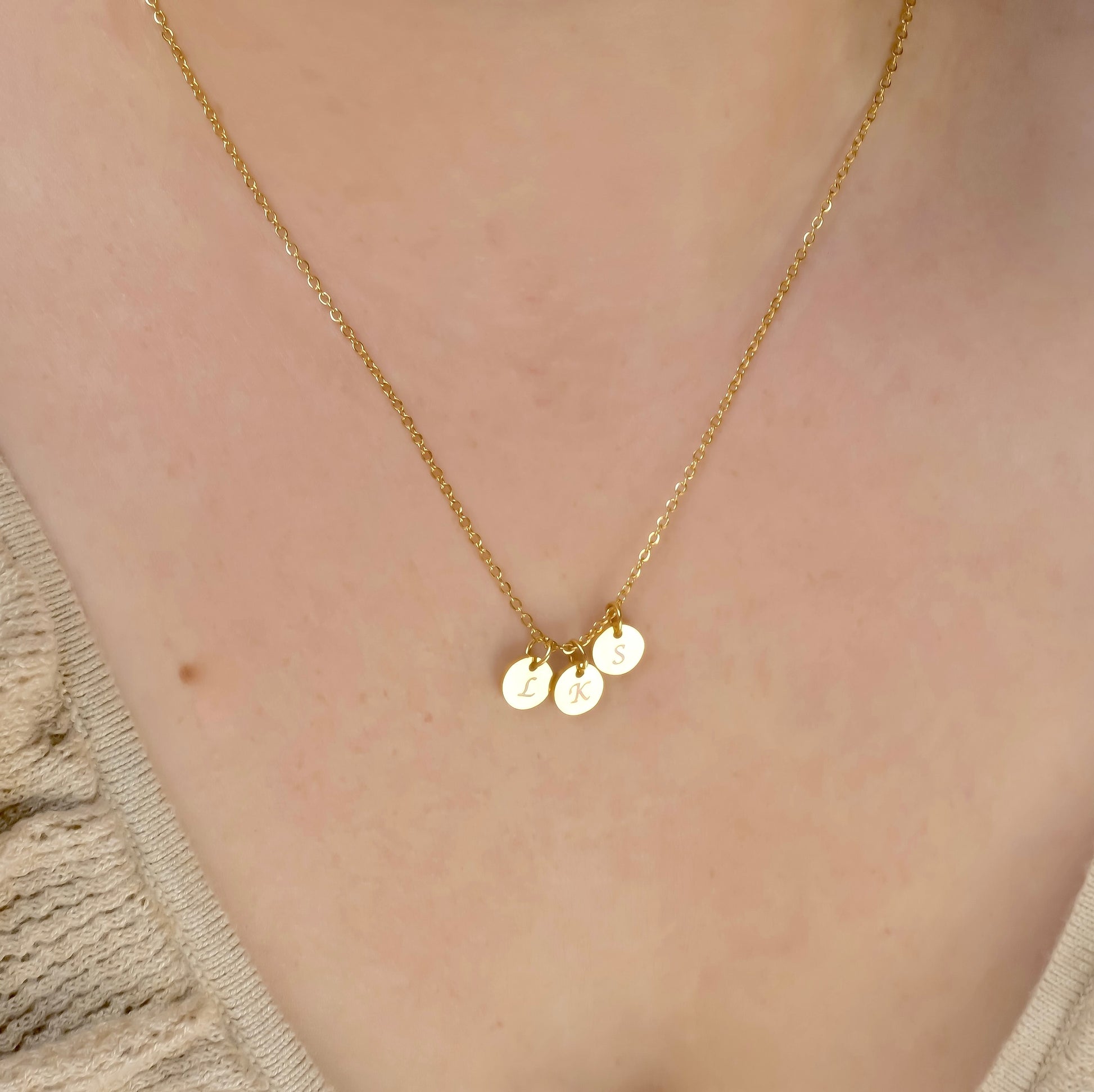 Gold necklace with three disc pendants reflecting light on a person wearing a beige top.