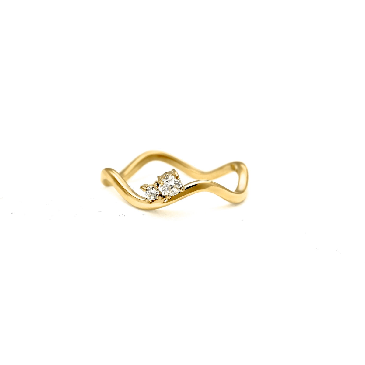 A gold ring with a wavy, flowing band and a small cluster of clear gemstones at the center, photographed on a plain white background.