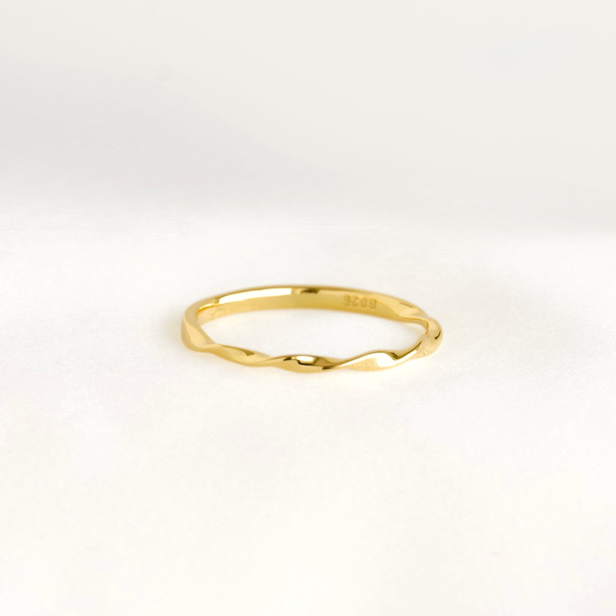 A thin gold ring with a wavy, organic twisted band design, photographed on a clean white background.