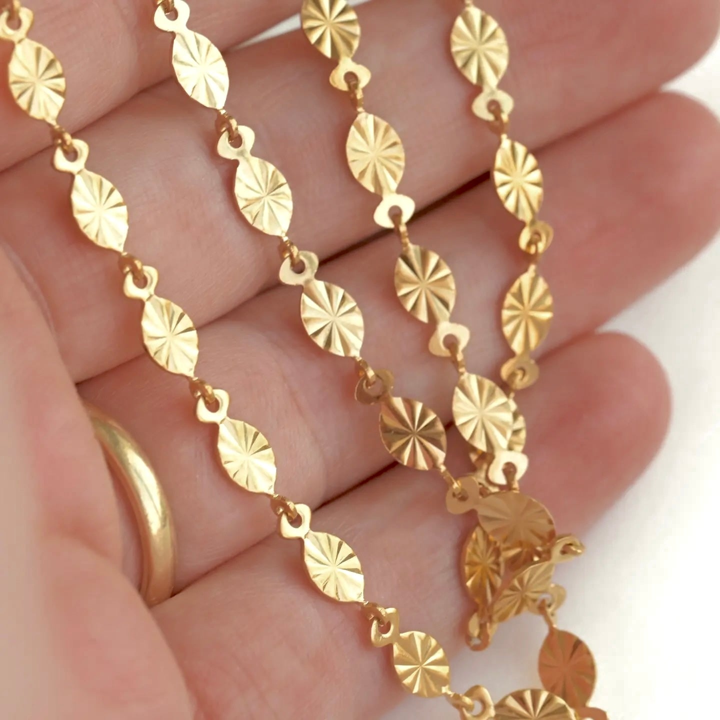 A close-up of a gold chain necklace with textured, starburst-patterned oval links draped over a person's hand.