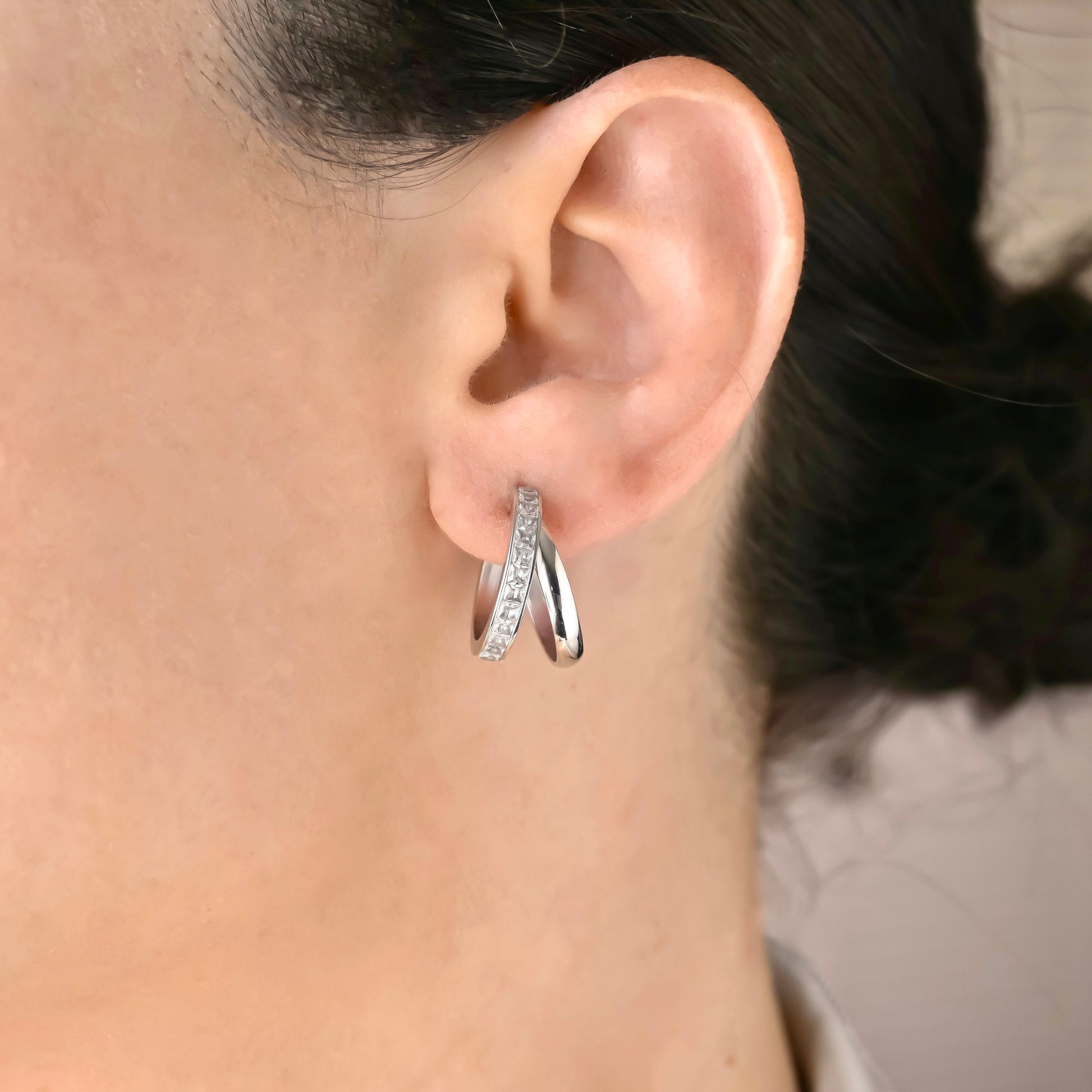 Close-up of an ear wearing a silver stacked hoop earring with small square  stones.