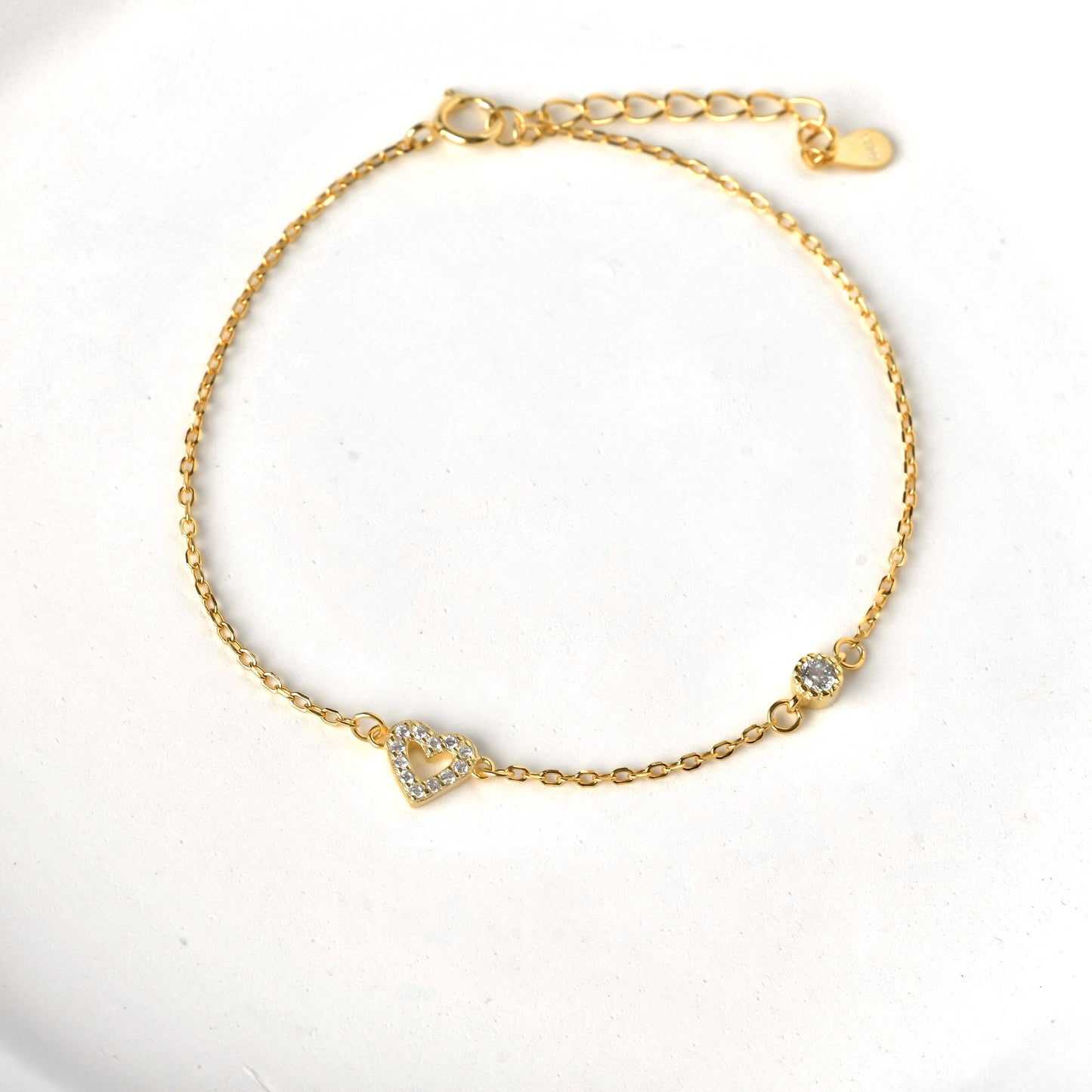 Gold pave heart bracelet with a single round stone on a white background