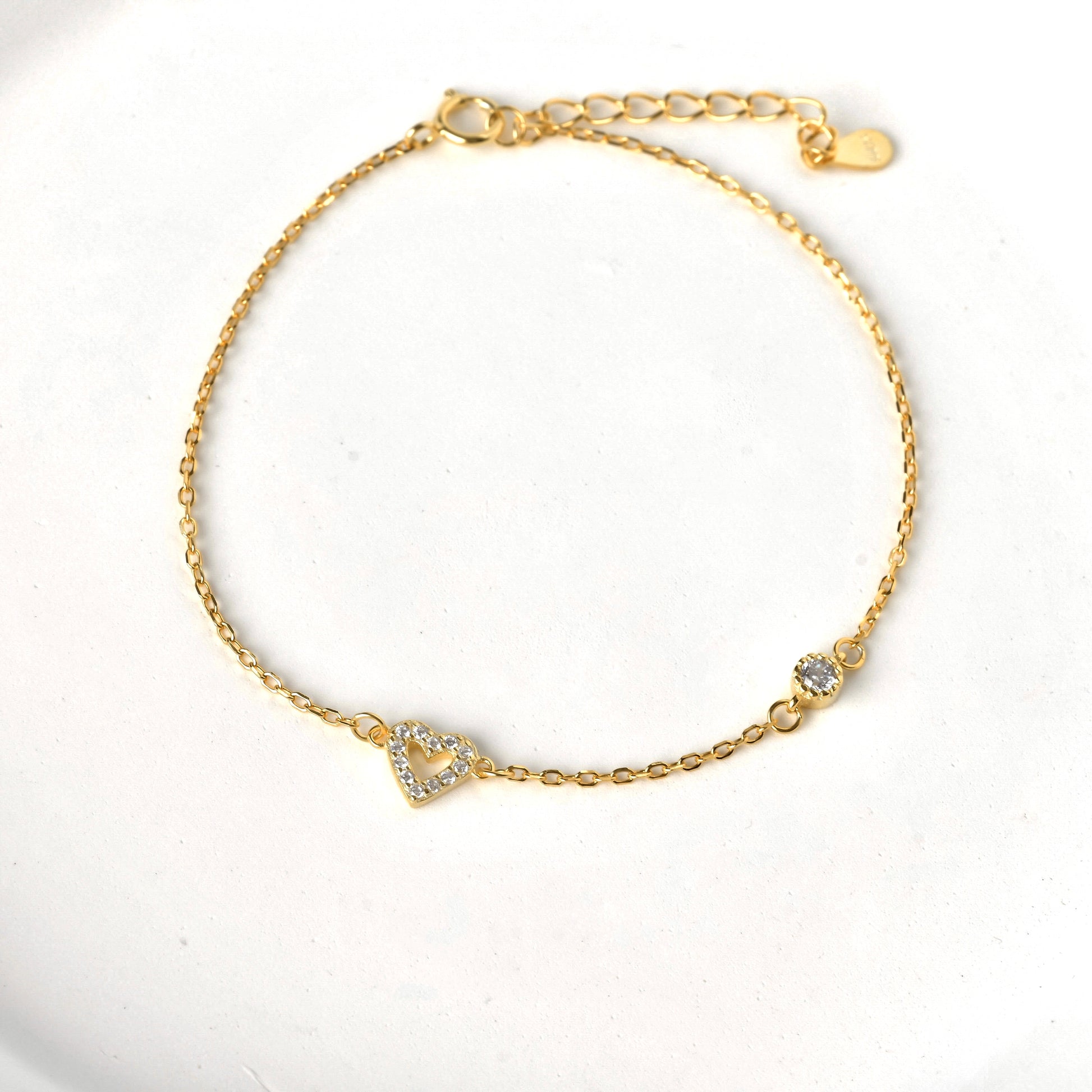 Gold pave heart bracelet with a single round stone on a white background