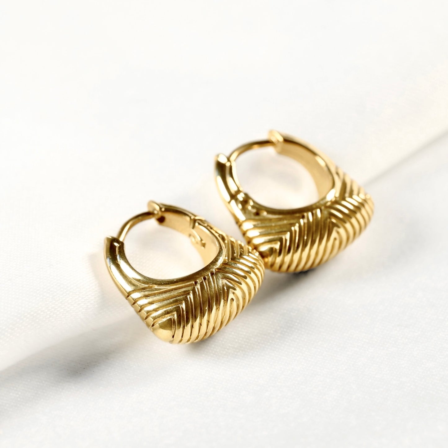 A pair of textured gold huggie hoop earrings with a ribbed, leaf-like pattern, displayed on a clean white surface.