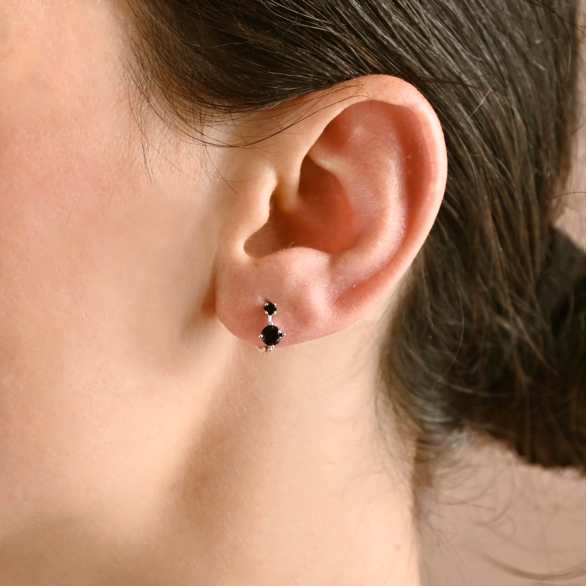 Close-up of an ear wearing a black gemstone stud earring with blurred background