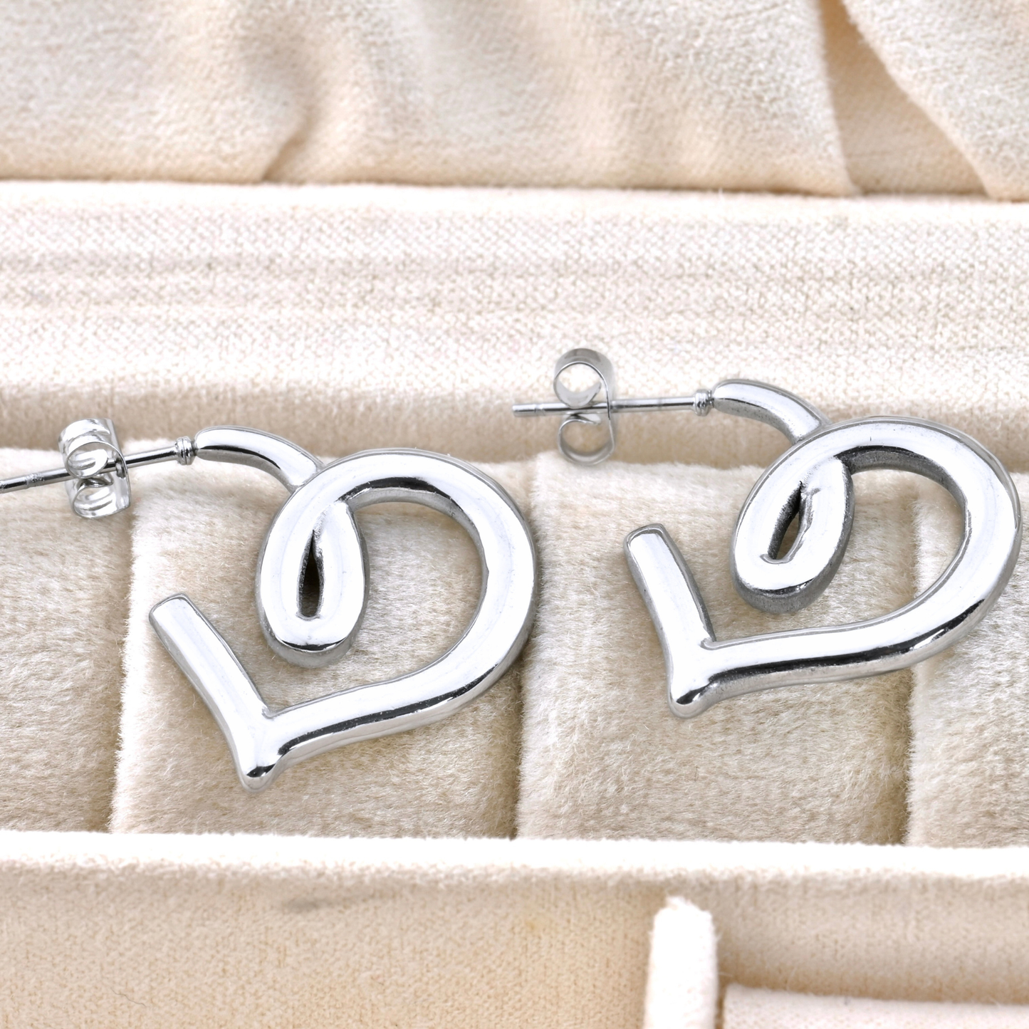 Silver heart figure earrings on a beige fabric background