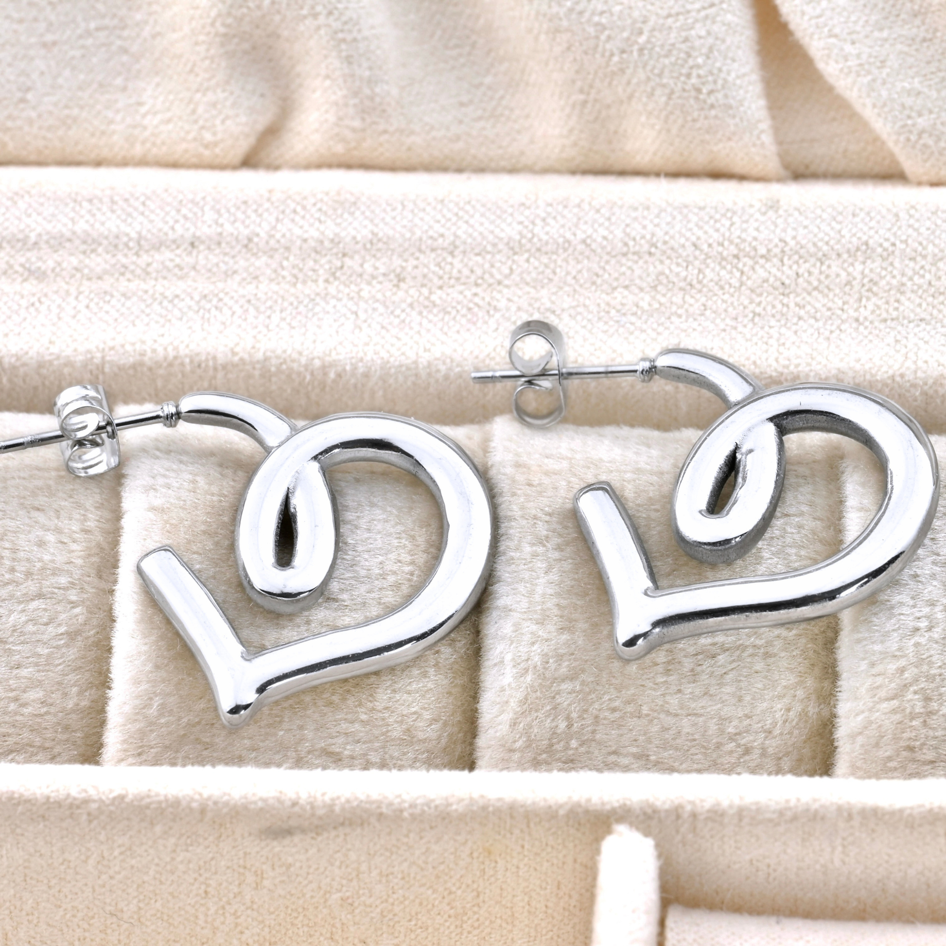 Silver heart figure earrings on a beige fabric background