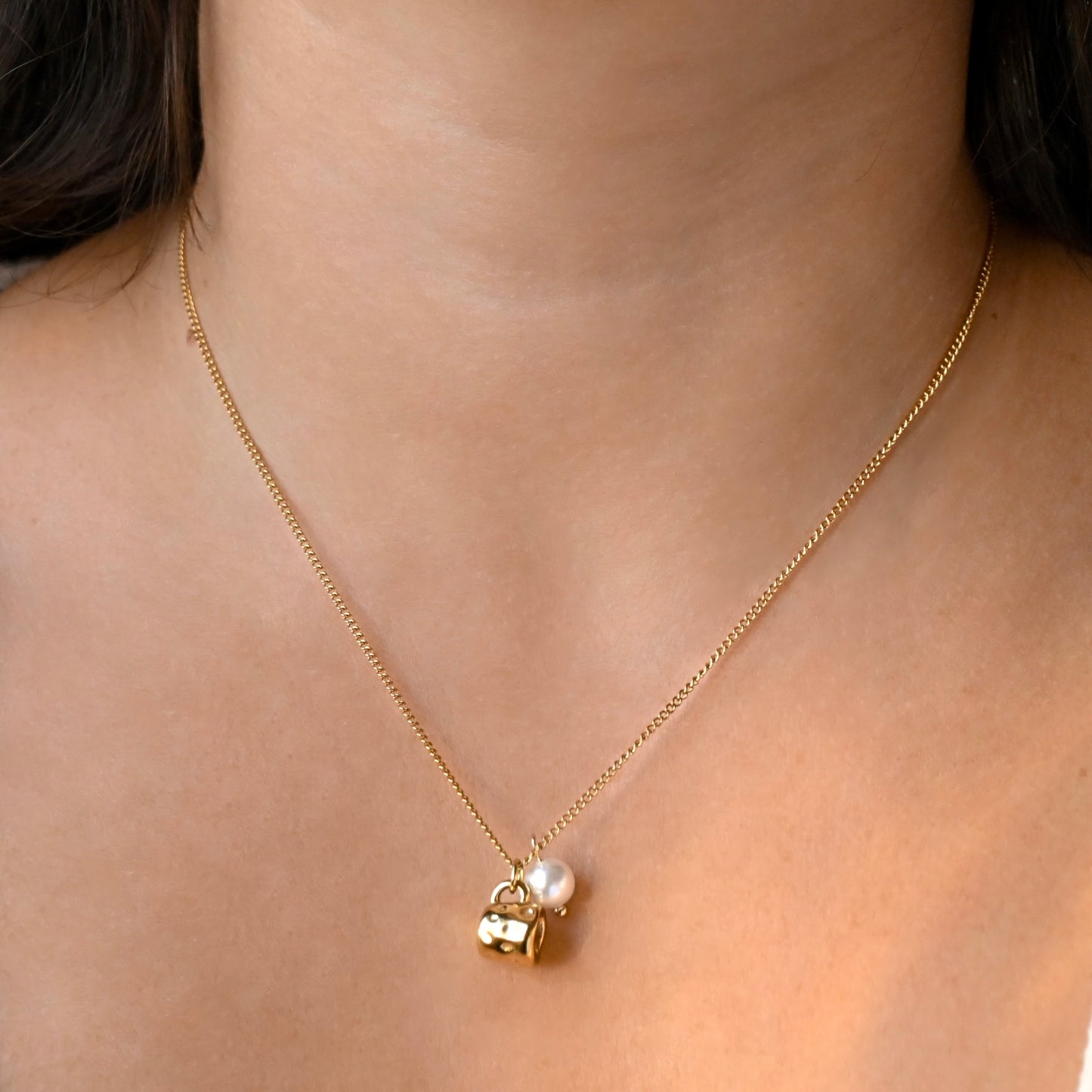 A delicate gold chain necklace worn on a model's neck, featuring a small gold coffee cup charm with a white pearl accent.