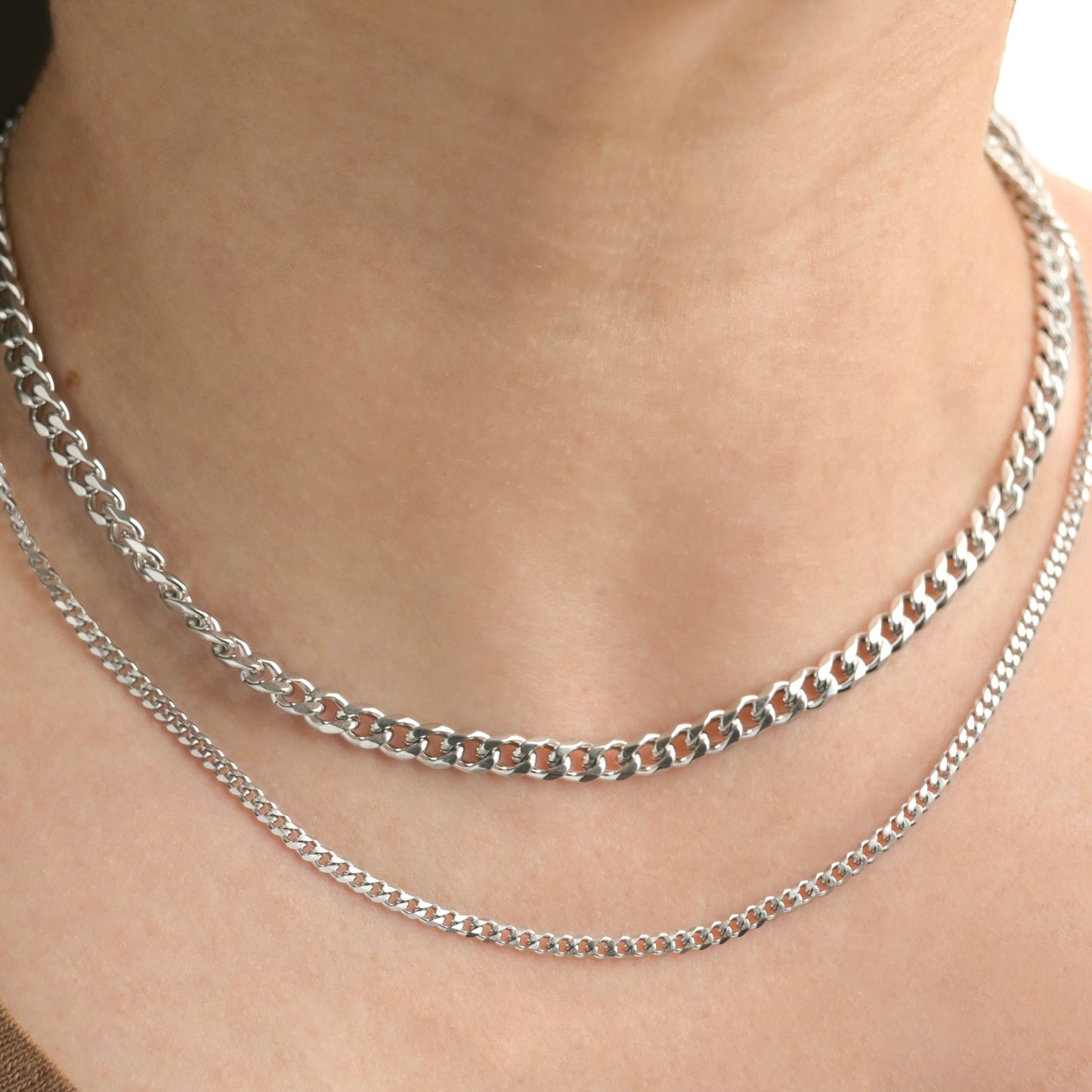 Front view of layered silver chain necklaces on a person's neck