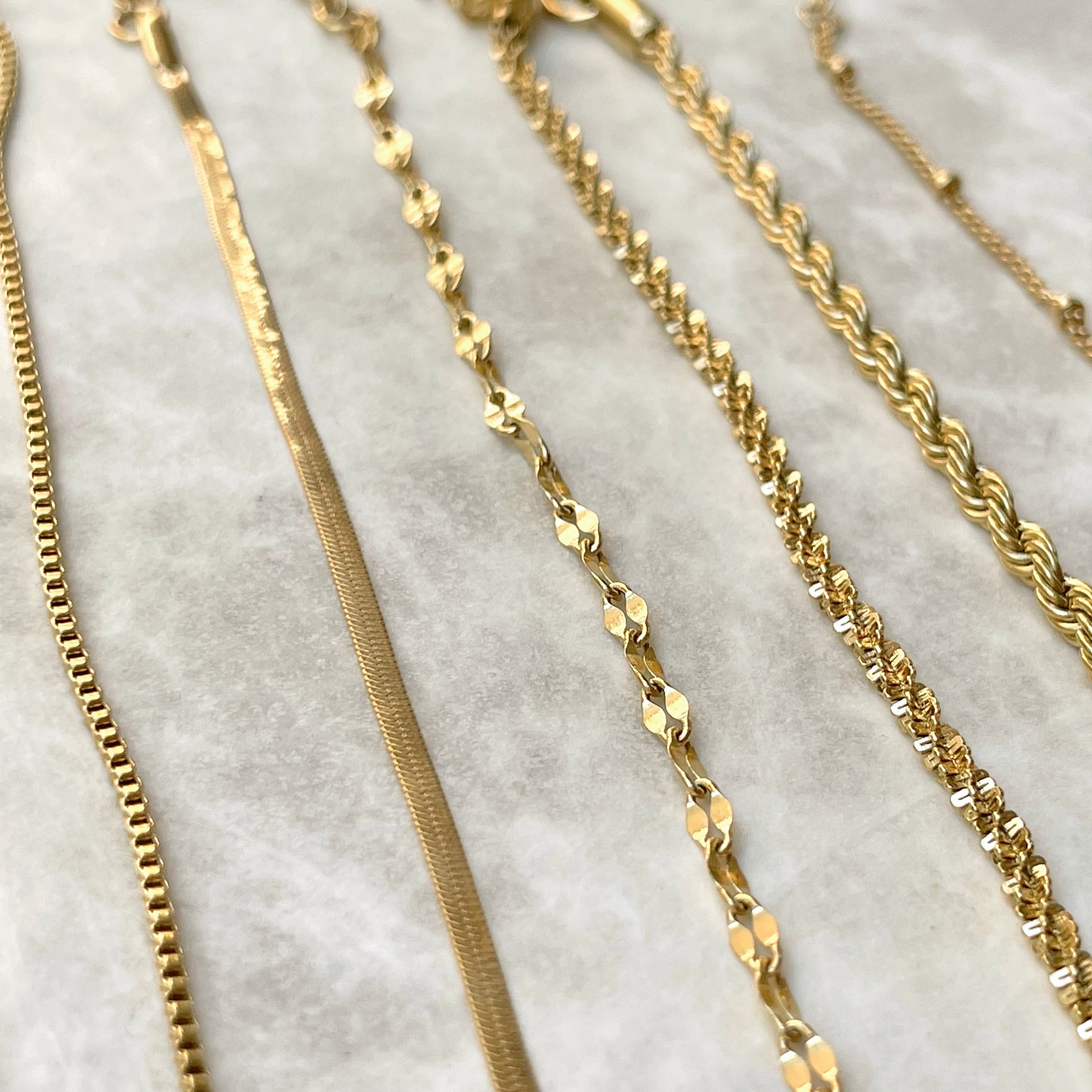 Close up view of gold chains of various designs vertically positioned on a marble surface