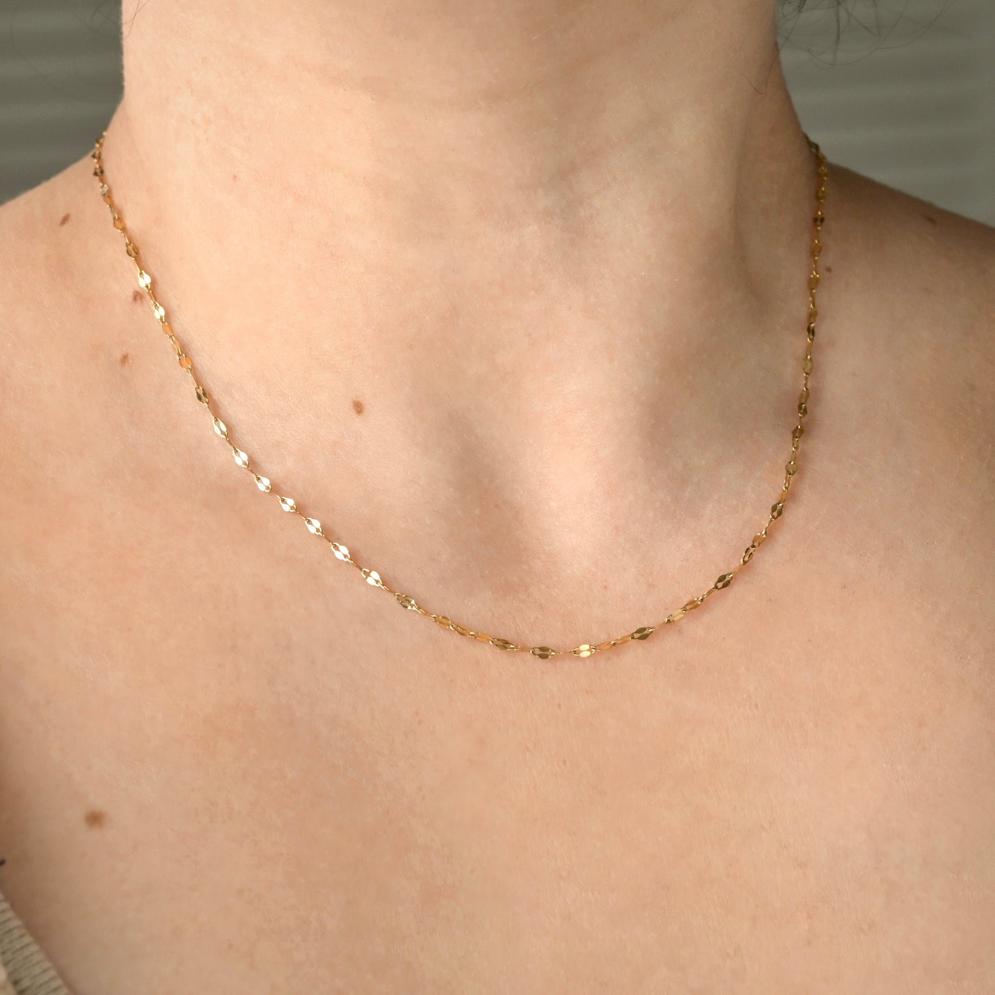 Dainty gold chain  on a person's neck with a neutral background
