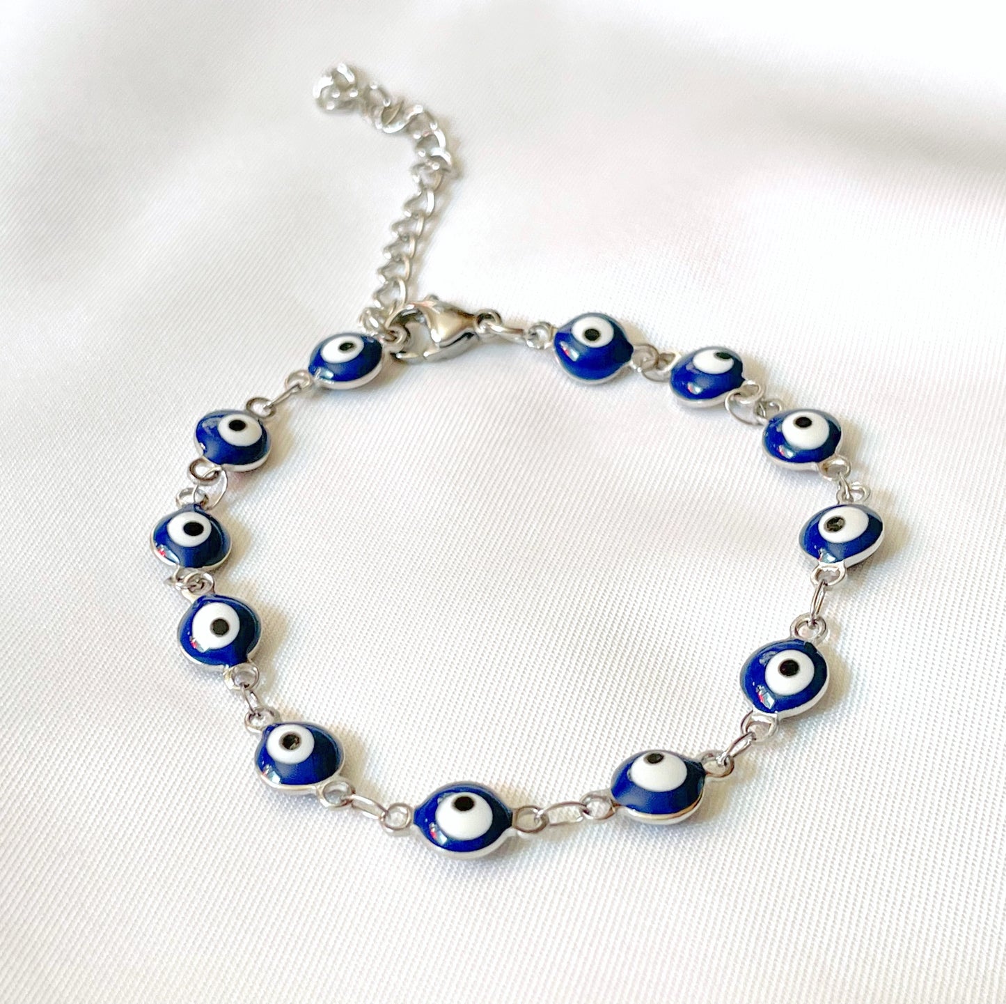 Silver bracelet with blue evil eye beads on a white fabric background