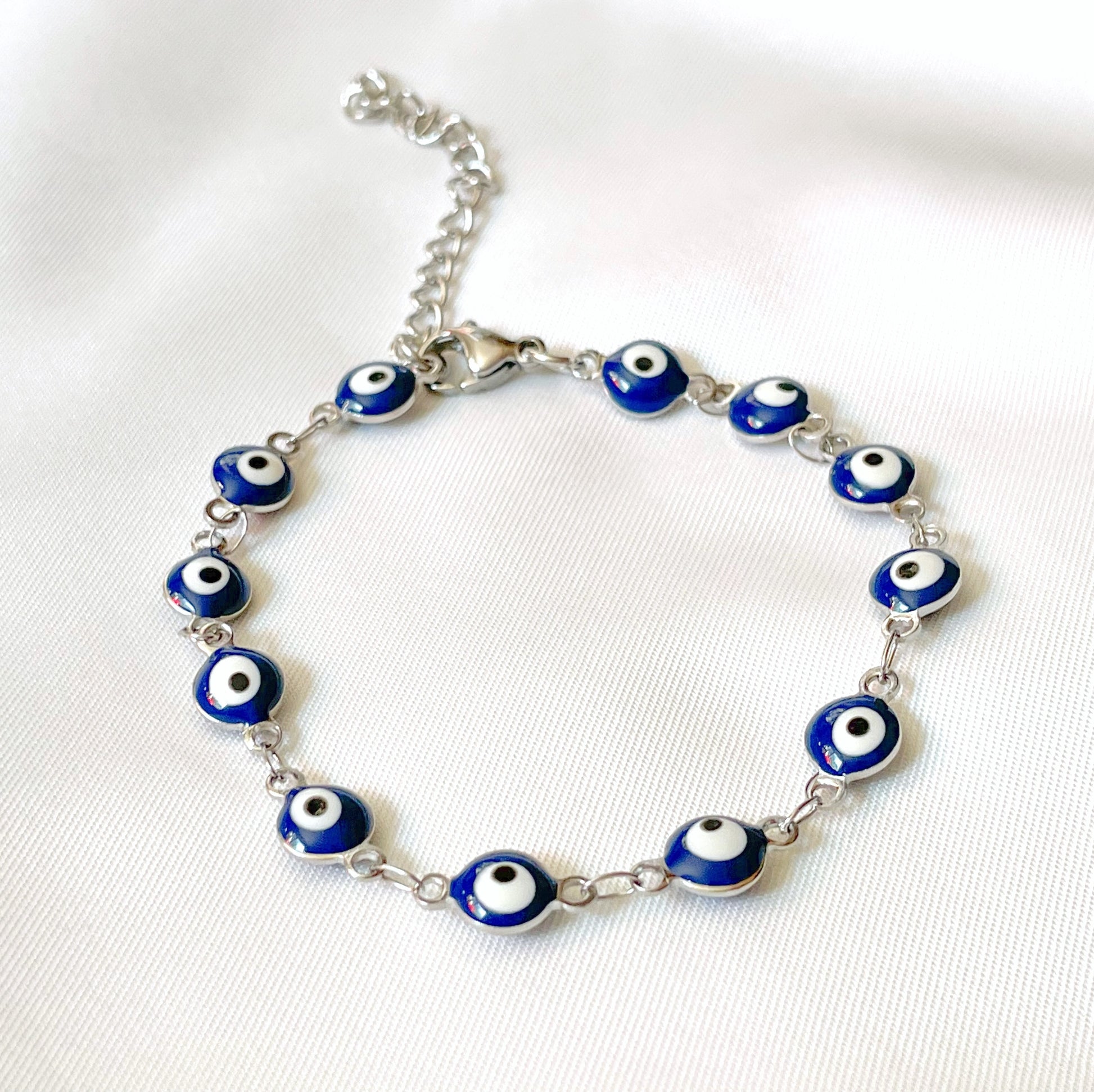 Silver bracelet with blue evil eye beads on a white fabric background