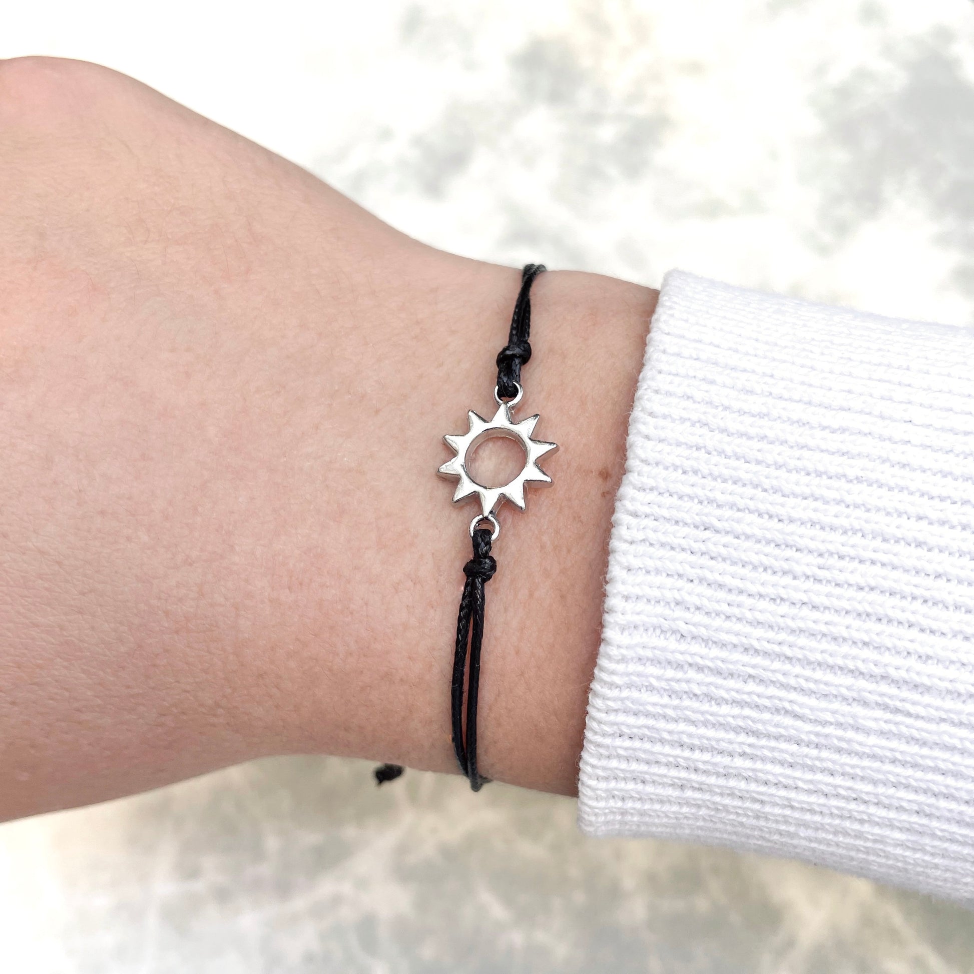 Wish bracelet with silver sun charm and black rope on a wrist against a white background