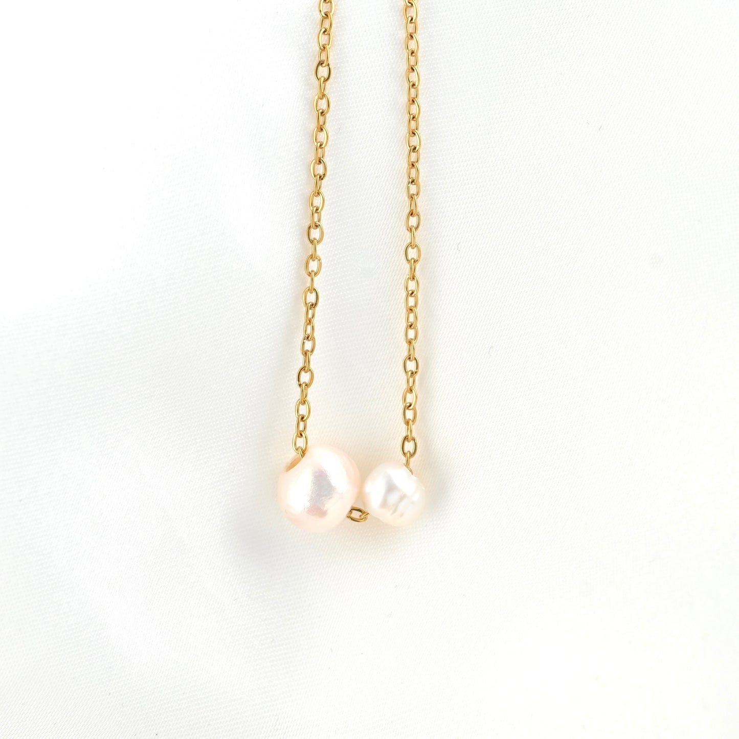 A delicate gold chain necklace featuring two small, irregular white freshwater pearls hanging from gold rings, displayed against a clean white background.