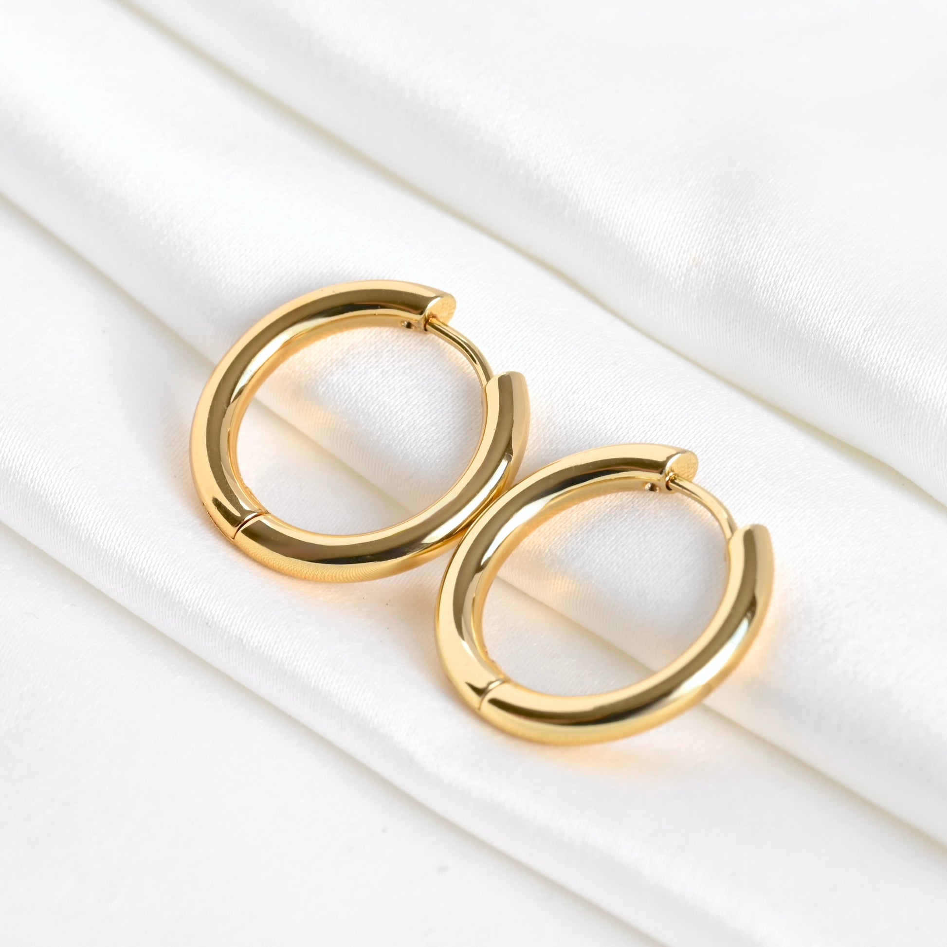Medium size hinged gold hoop earrings on a white surface