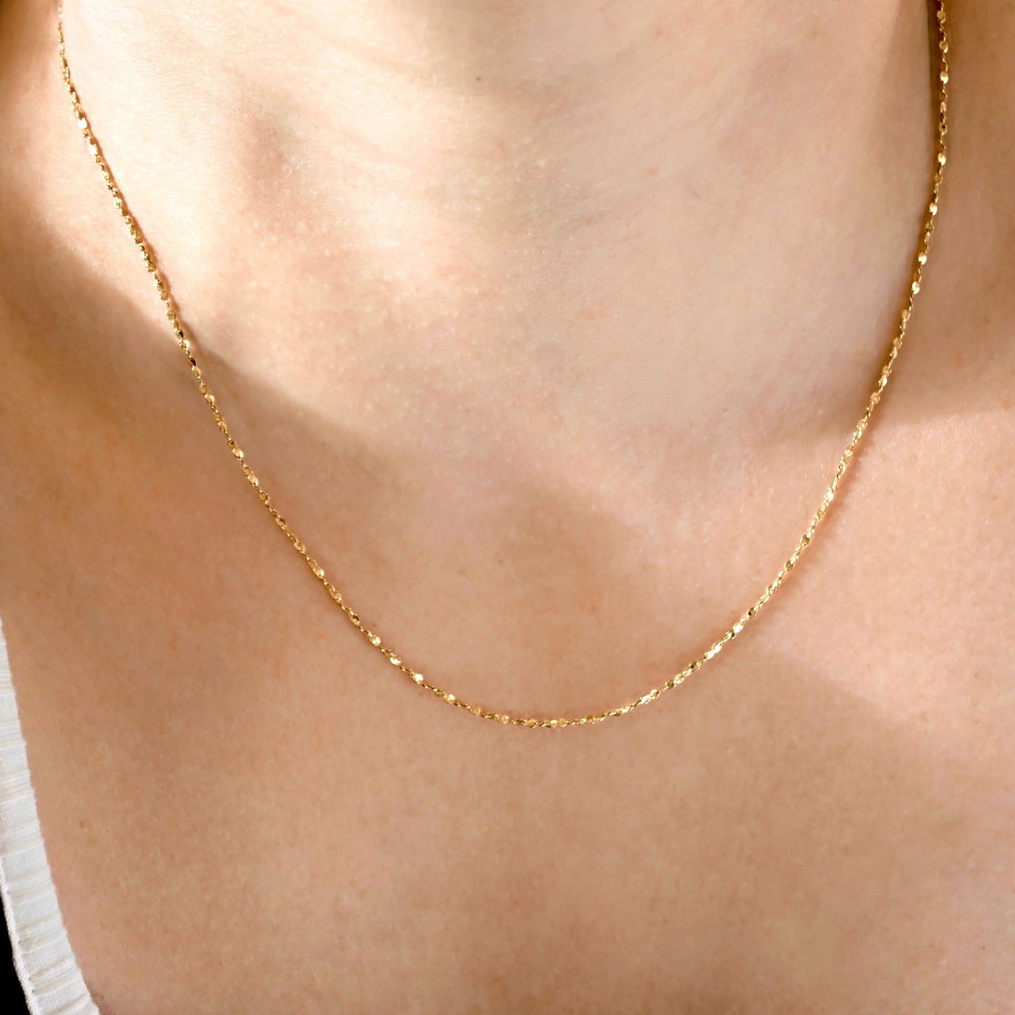 A delicate gold chain necklace worn on a person's neck, shown in a close-up shot with warm, natural lighting.