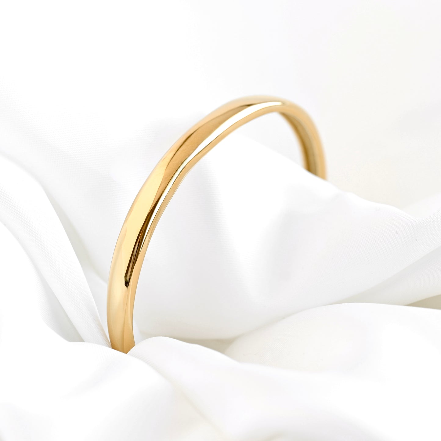 A polished gold bangle bracelet resting on draped white fabric.