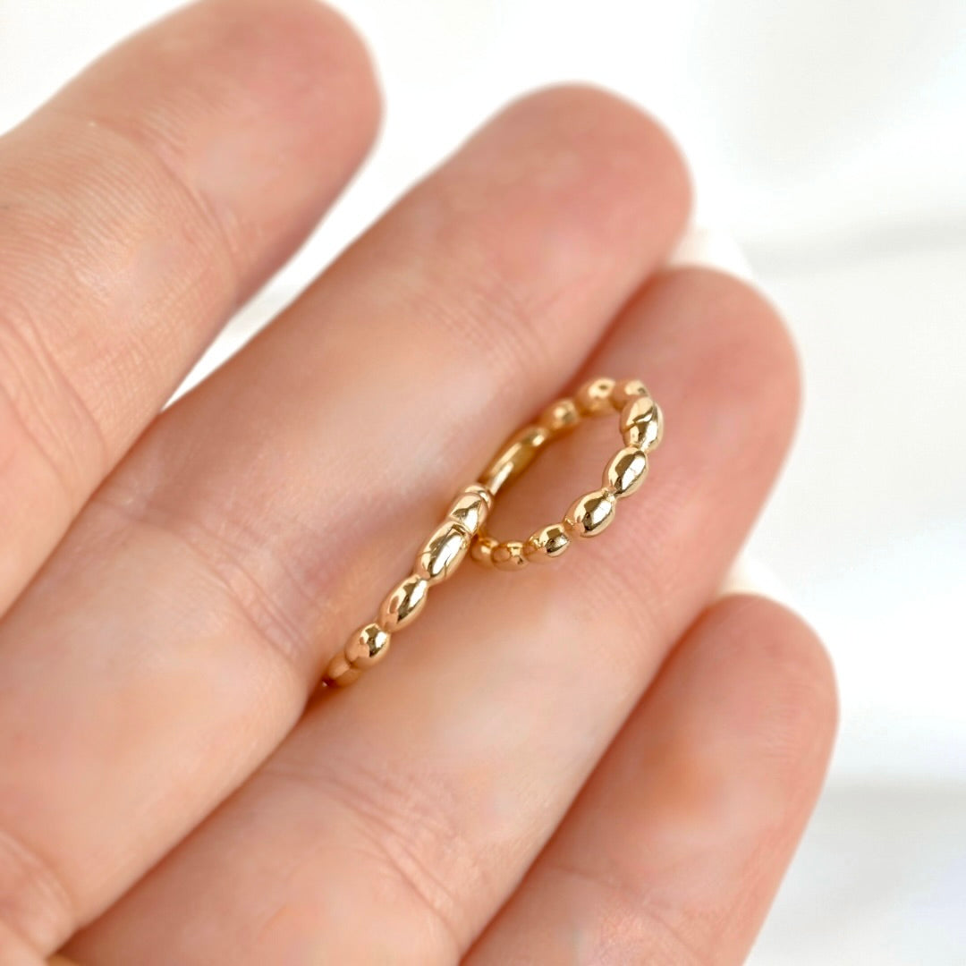 A pair of delicate gold hoops with a textured, beaded twisted design, shown worn on a person's finger against a soft white background.