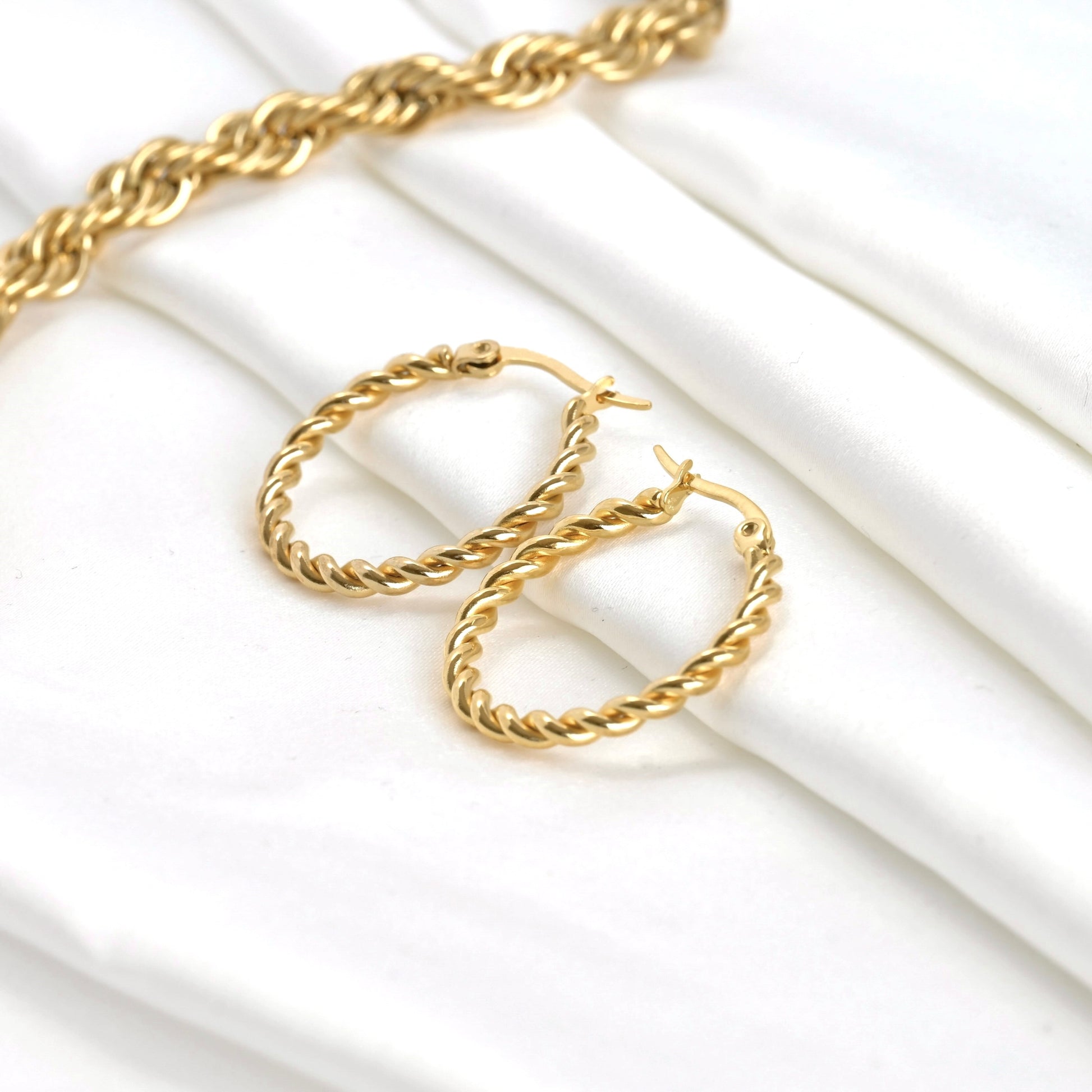 Thin gold hoop earrings on a white background with a thick rope chain in the corner