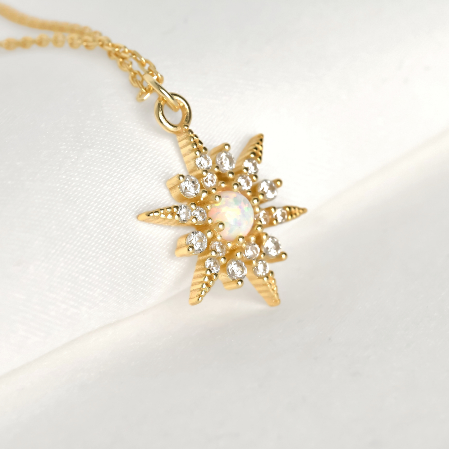 Gold north star pendant necklace with an opal centerpiece and smallar CZ stones around on a white background