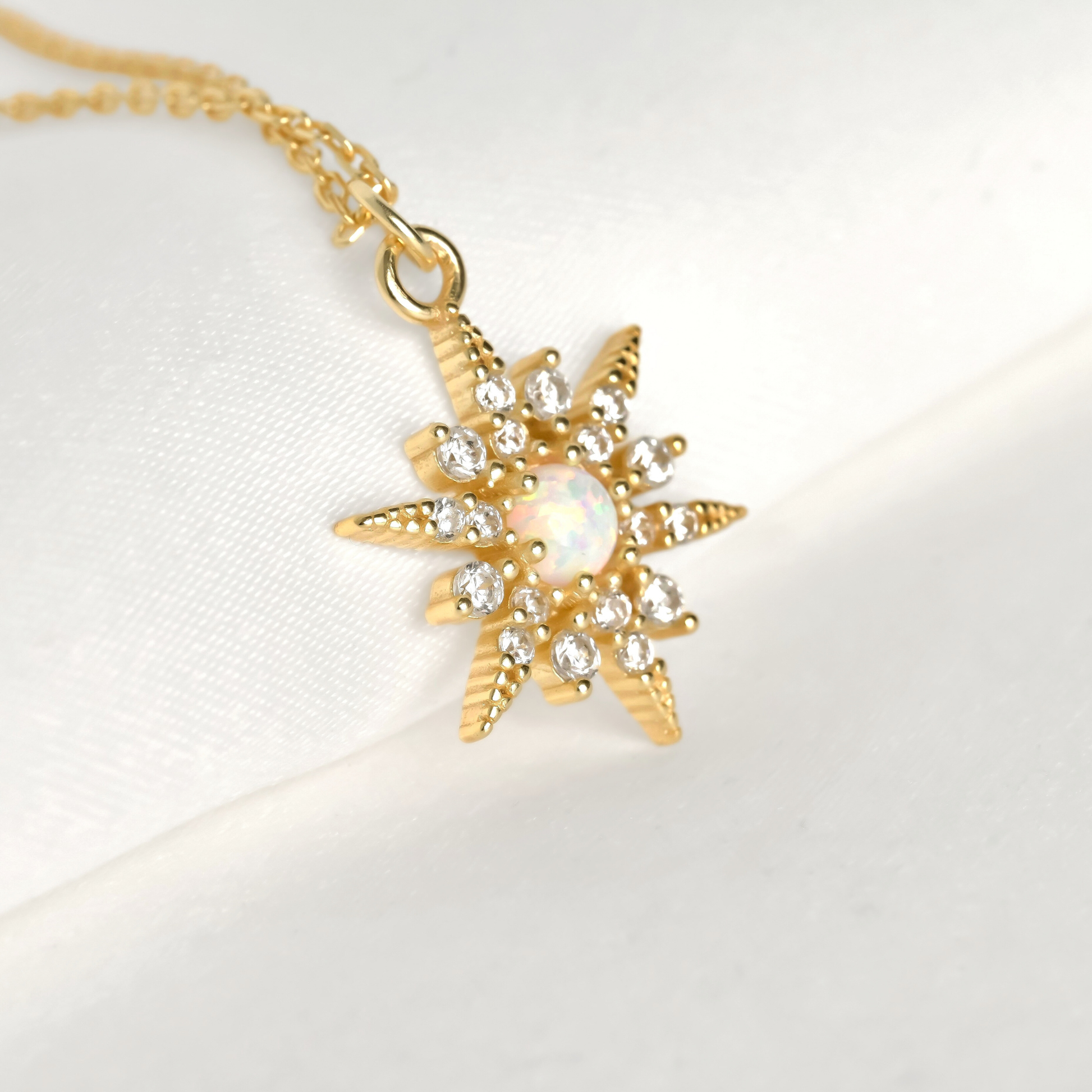 Gold north star pendant necklace with an opal centerpiece and smallar CZ stones around on a white background