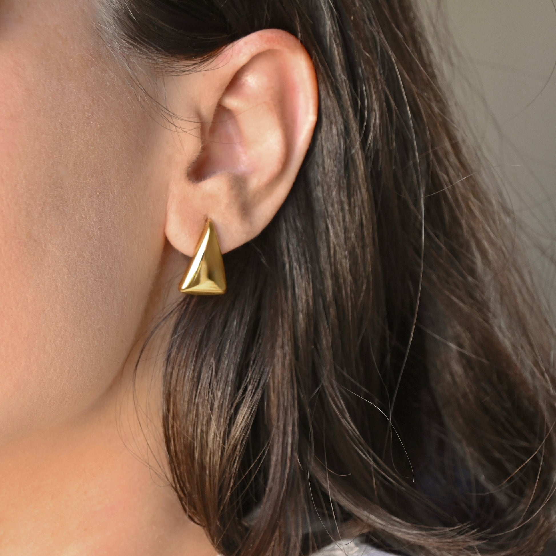 Gold triangle drop earring worn by a person with brown hair.