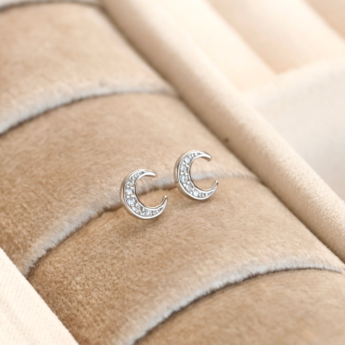 Silver moon-shaped earrings with embedded stones on a beige fabric background