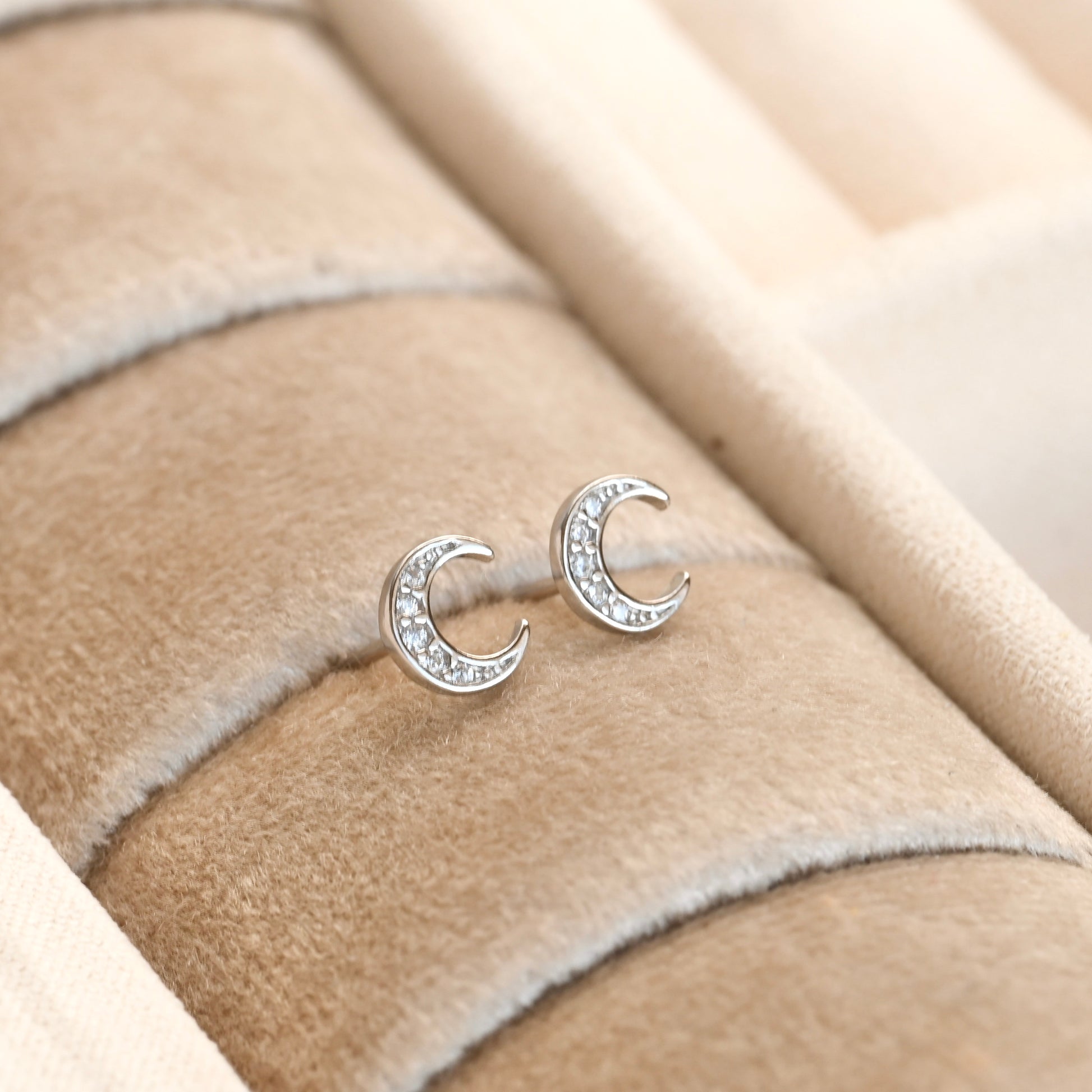 Silver moon-shaped earrings with embedded stones on a beige fabric background