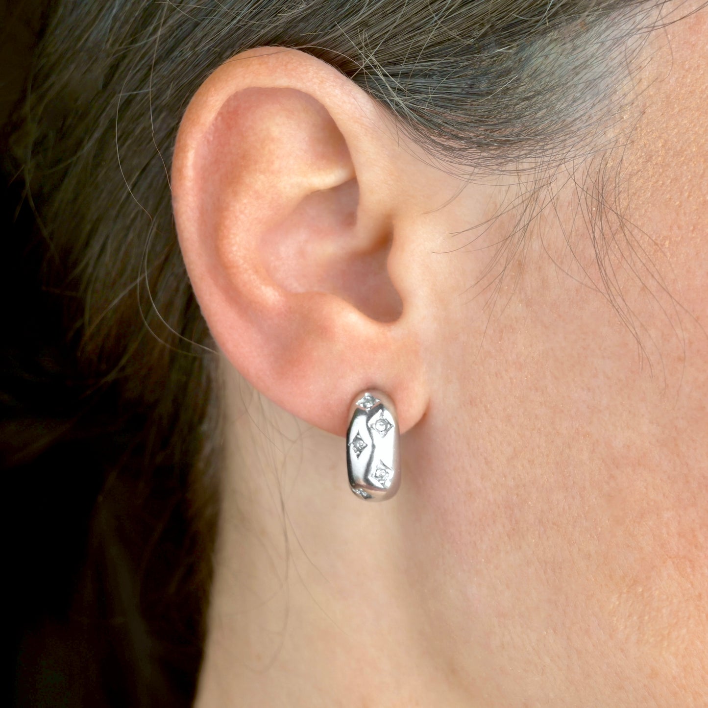 Close-up of an ear wearing a chunky silver hoop stud earrings with embedded CZ stones