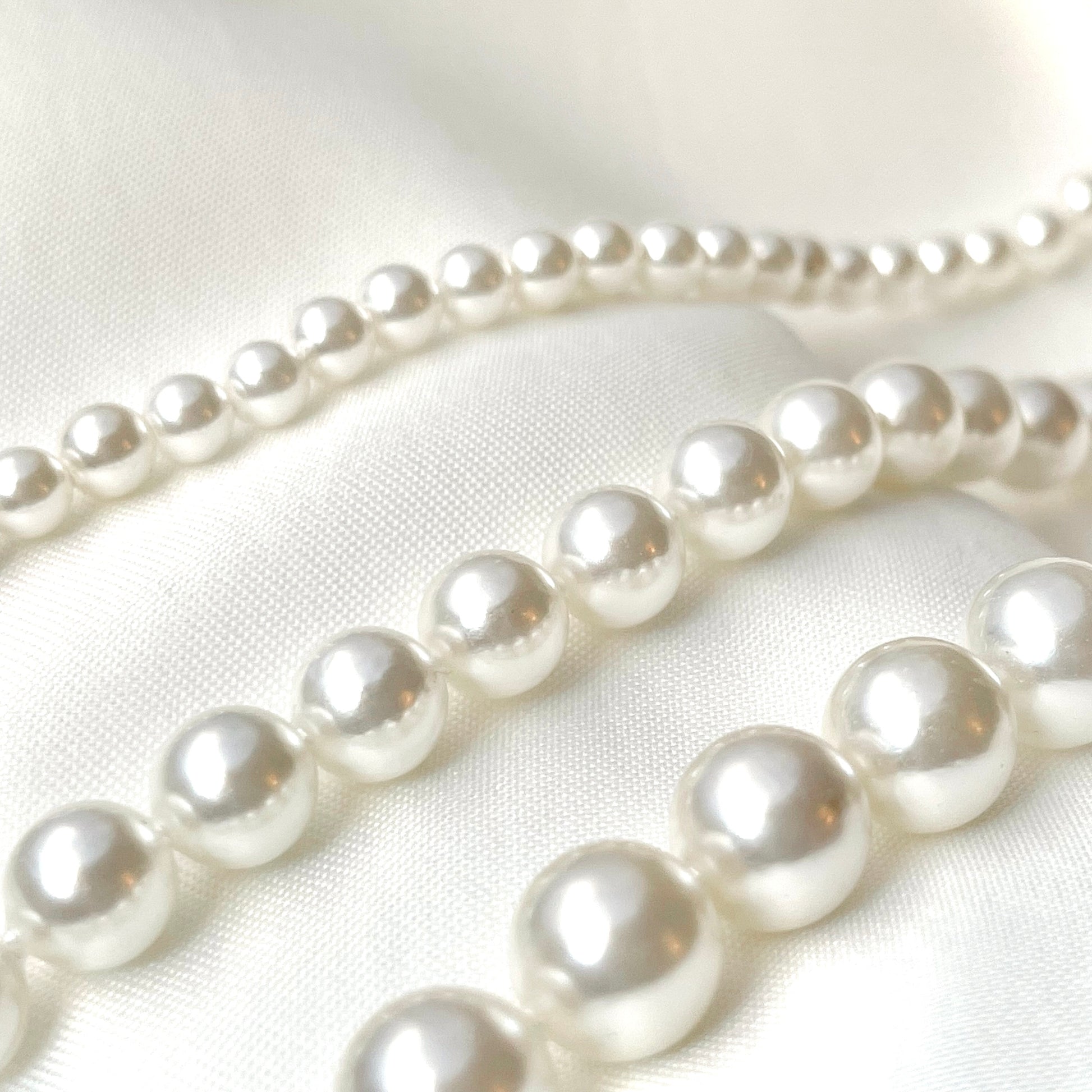 Three strands of pearls with 4, 6 and 8mm pearl sizes, on a white fabric background