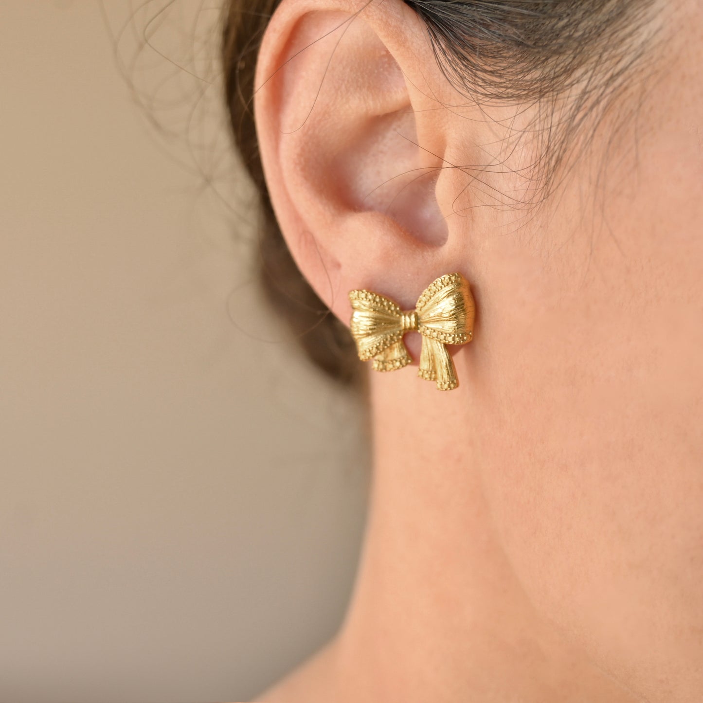Gold bow-shaped earring worn by a person with a neutral background