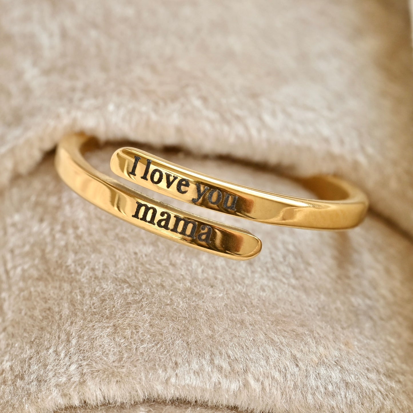 Gold open ring with 'I love you mama' engraving on a soft beige background