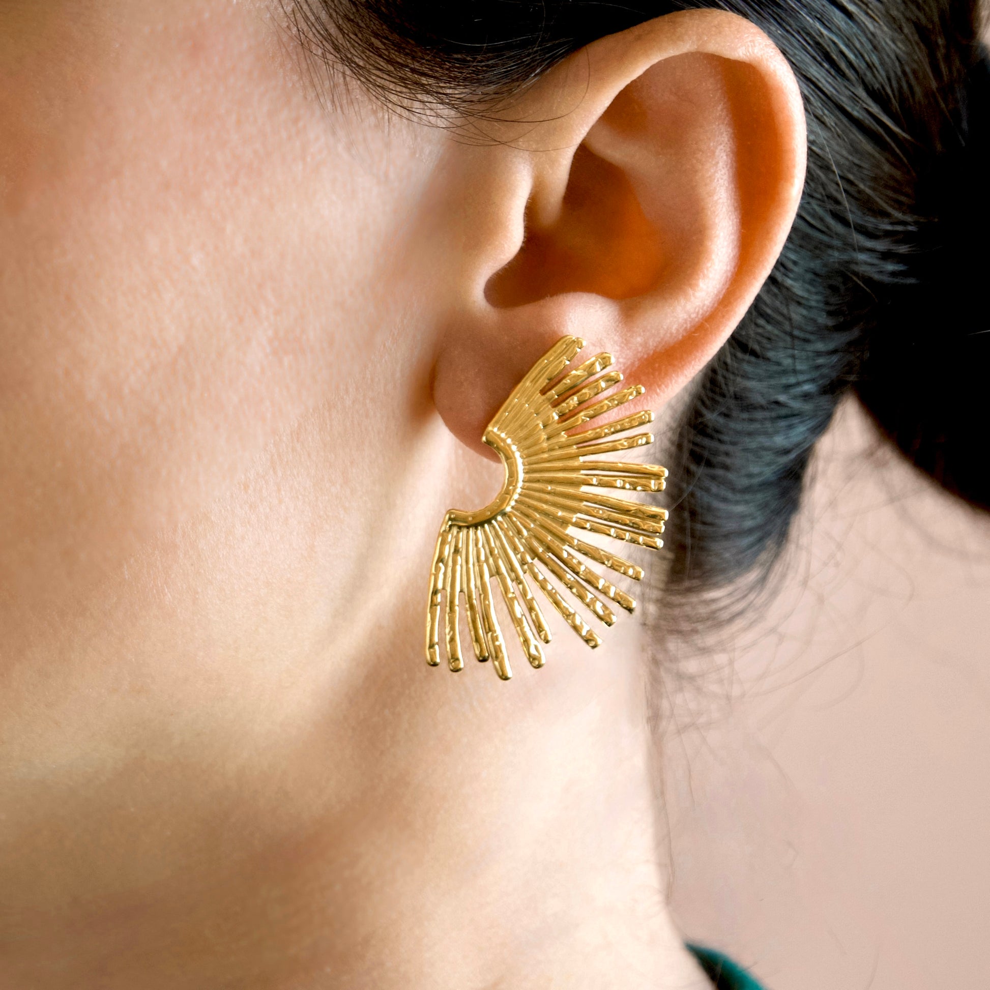 A close-up of a model's ear wearing a large gold sunburst stud earring.