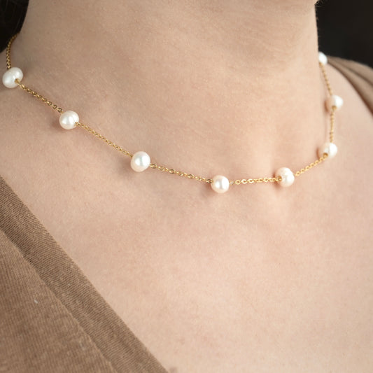 Pearl station necklace with gold chain on a person wearing a brown top