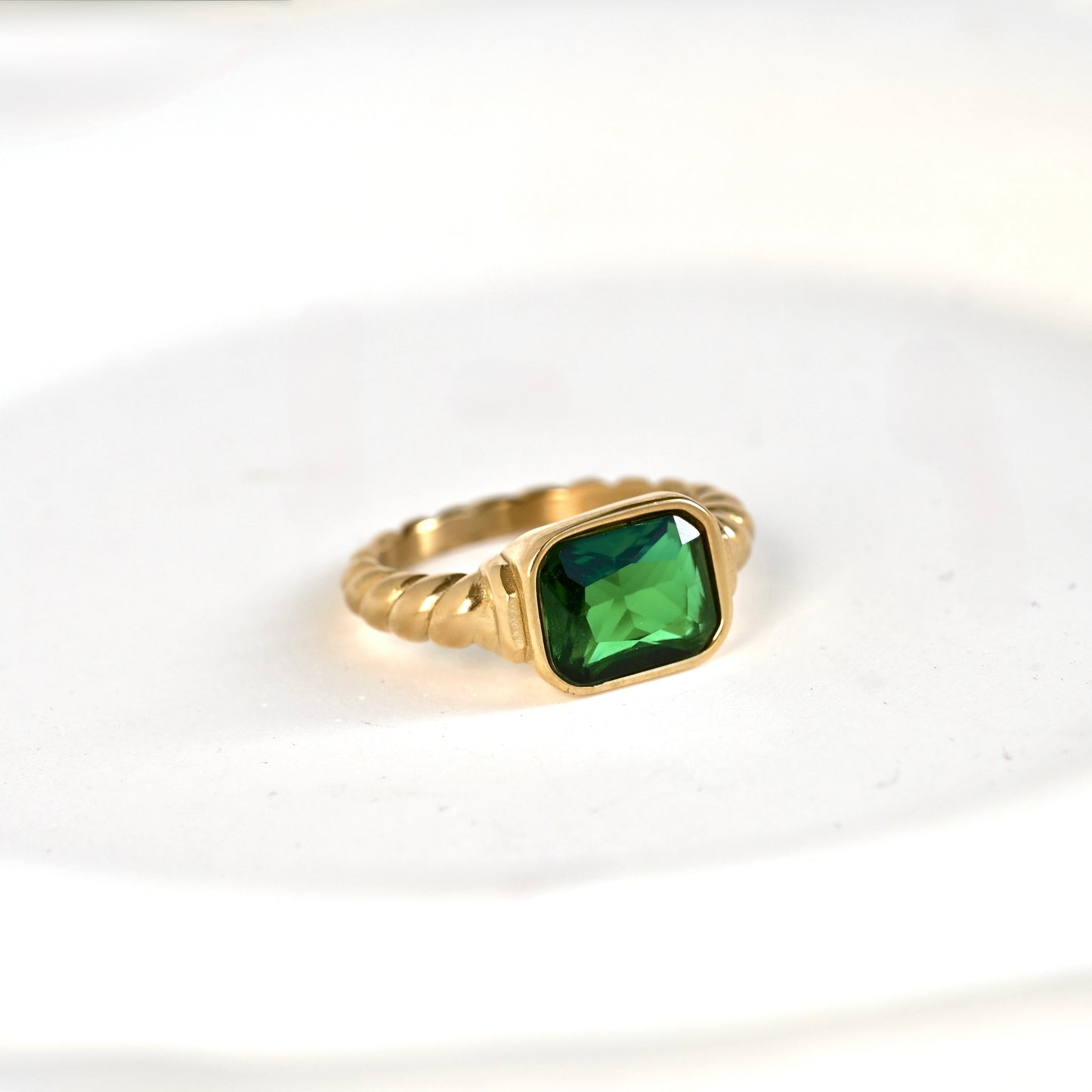 A gold  signet ring featuring a square-cut green gemstone, set against a clean white background.