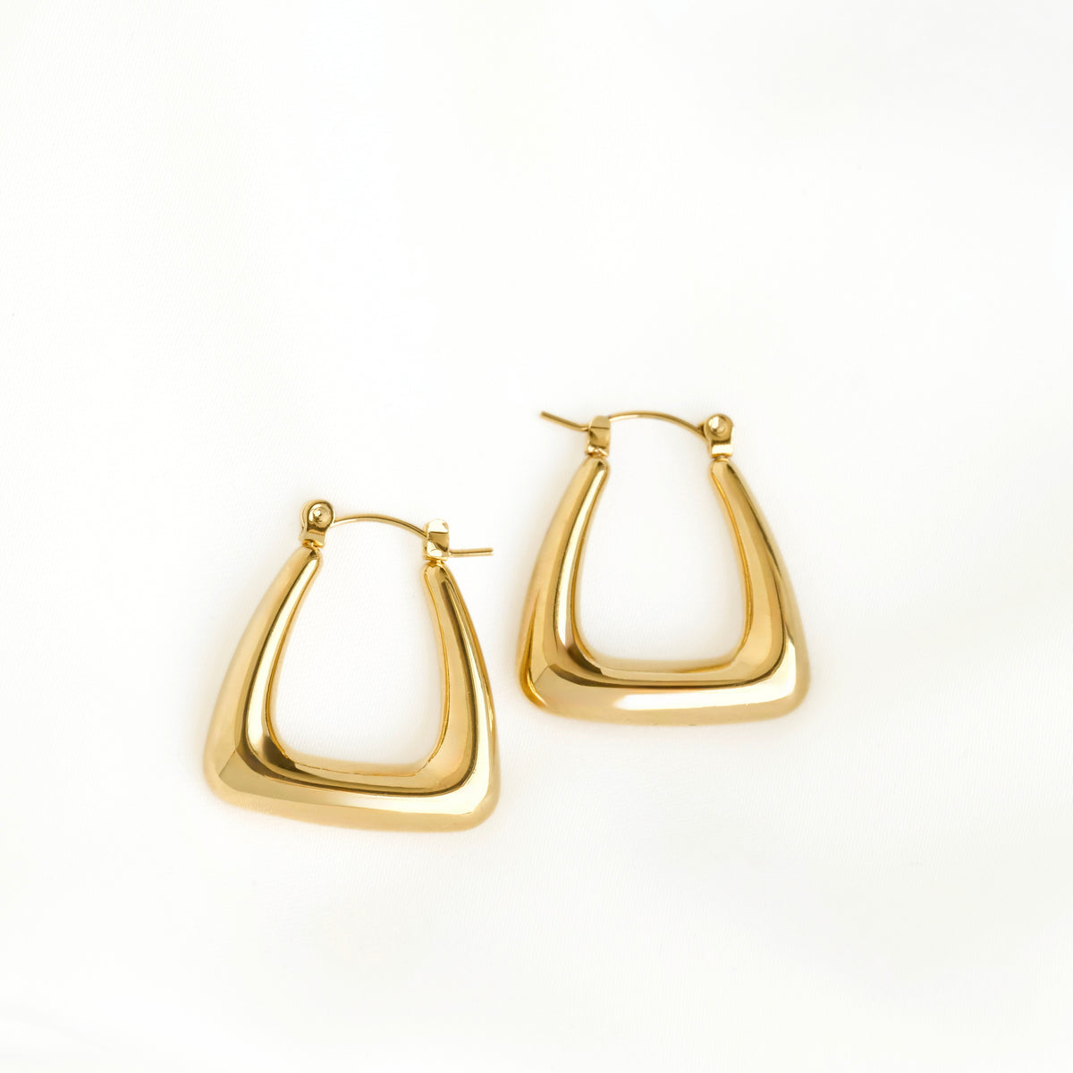 A pair of polished gold-tone geometric triangular hoop earrings with a thick, rounded triangular shape, displayed on a clean white background.