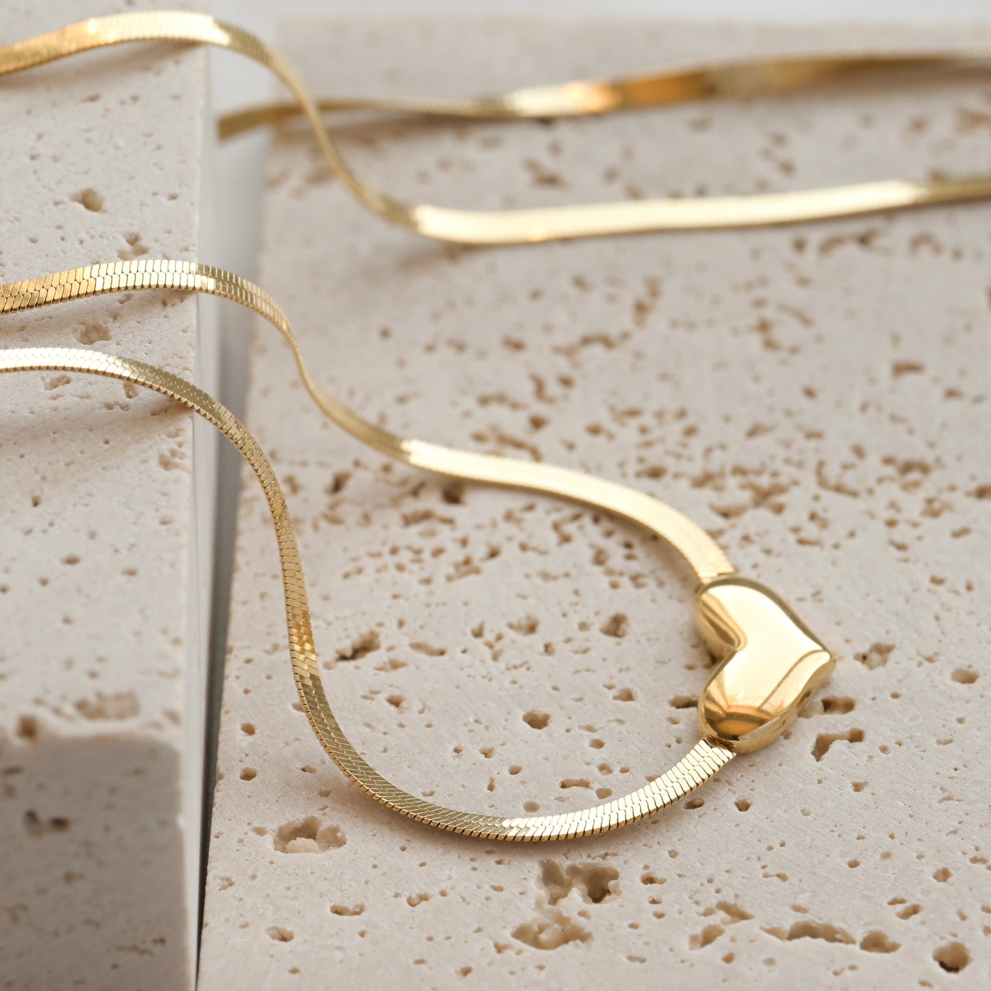 Gold flat herringbone necklace on a textured beige surface