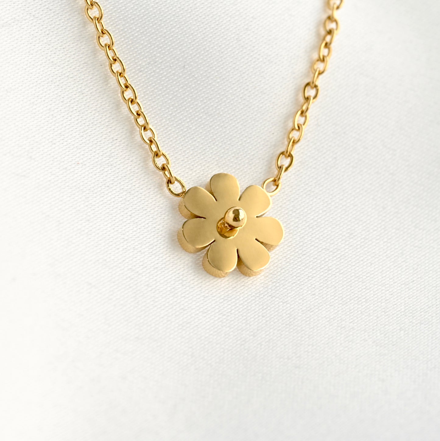 Tiny gold flower-shaped pendant on a chain against a white background