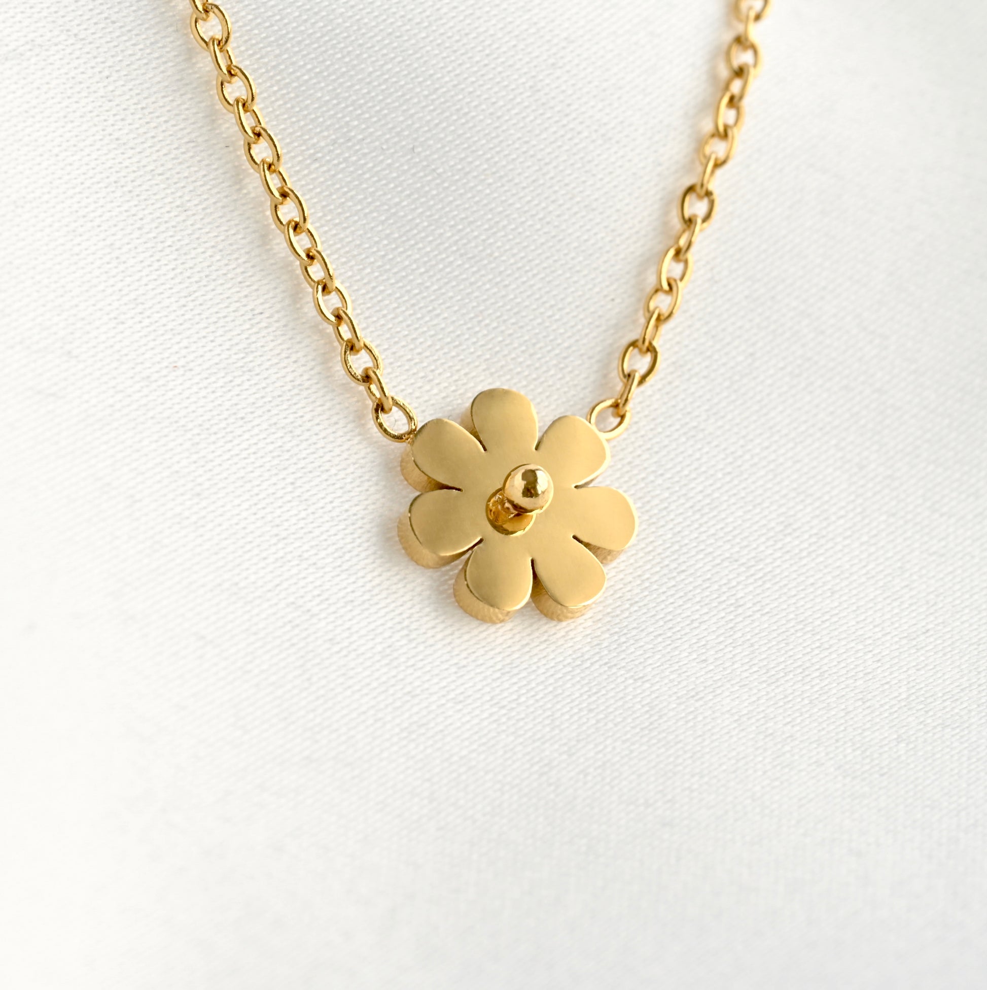 Tiny gold flower-shaped pendant on a chain against a white background